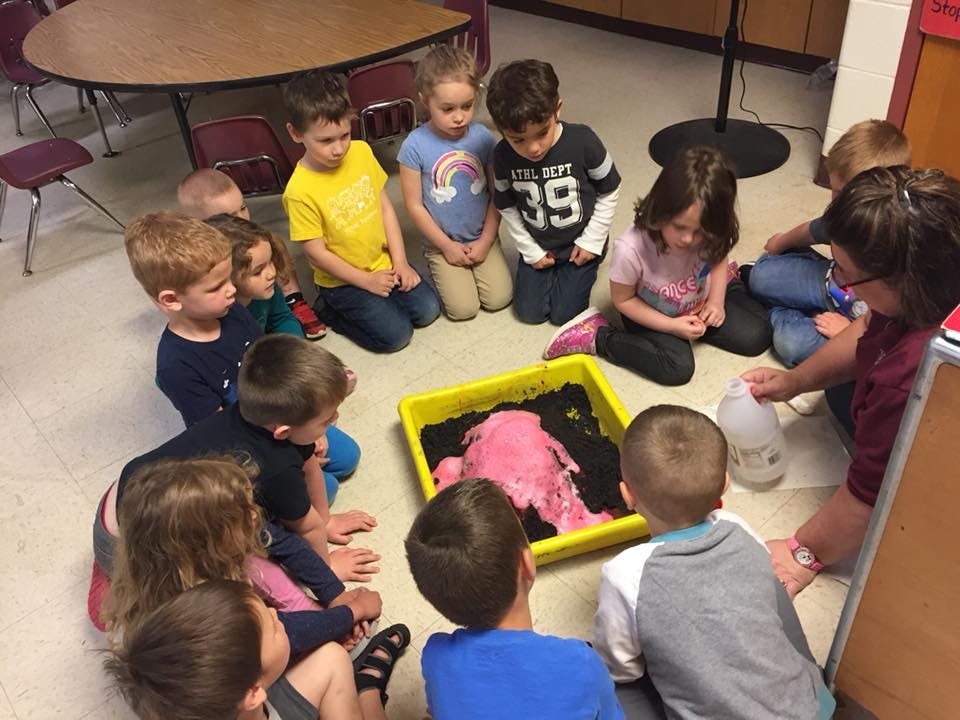 Children and an adult watching a pink volcano eruption in a tray