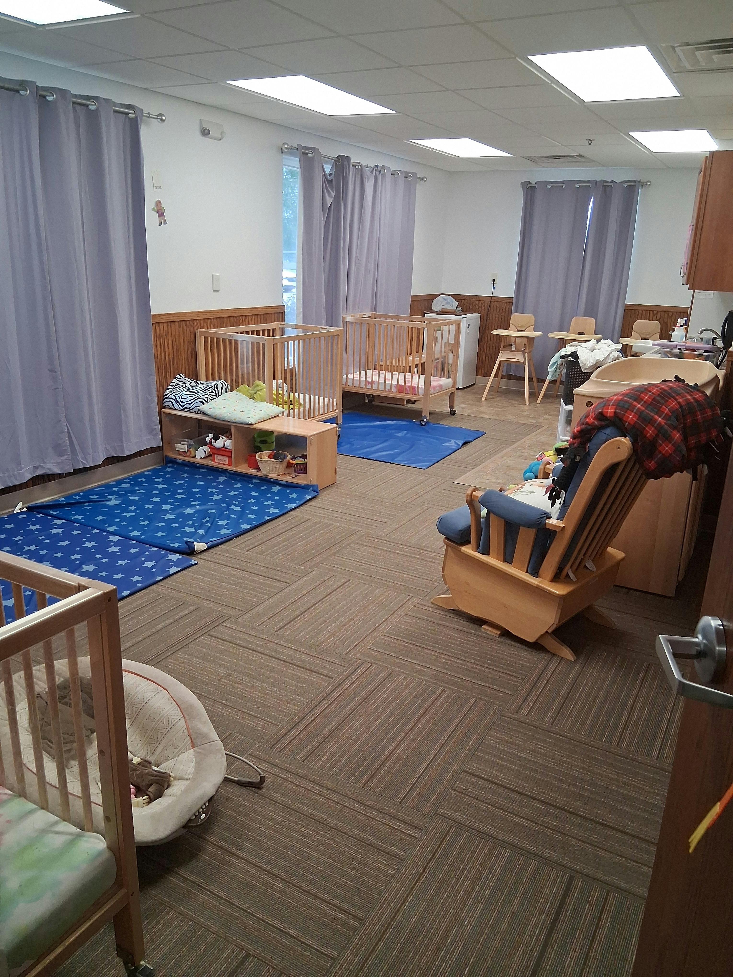 Nursery room with multiple cribs, blue mats, and a rocking chair
