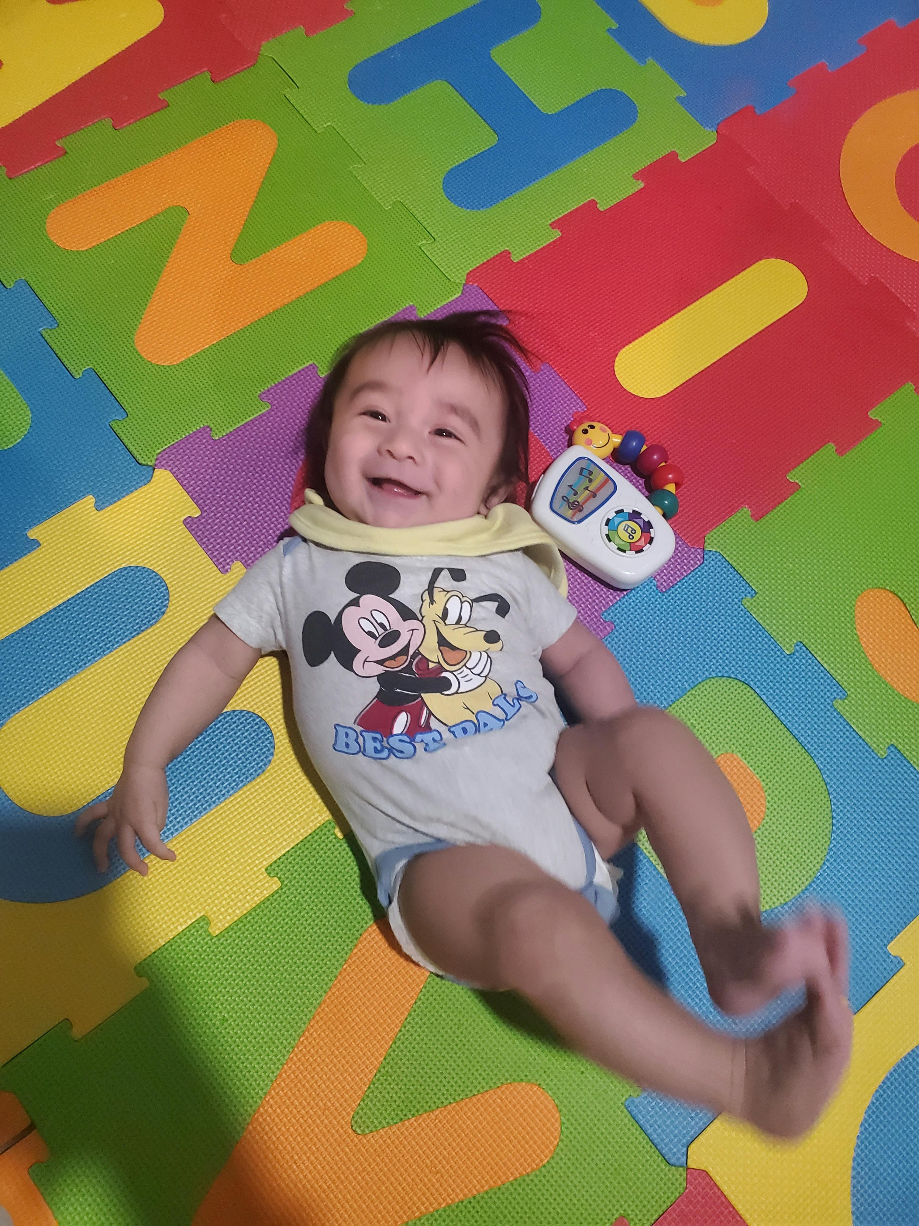 Child lying on a colorful alphabet playmat with a toy