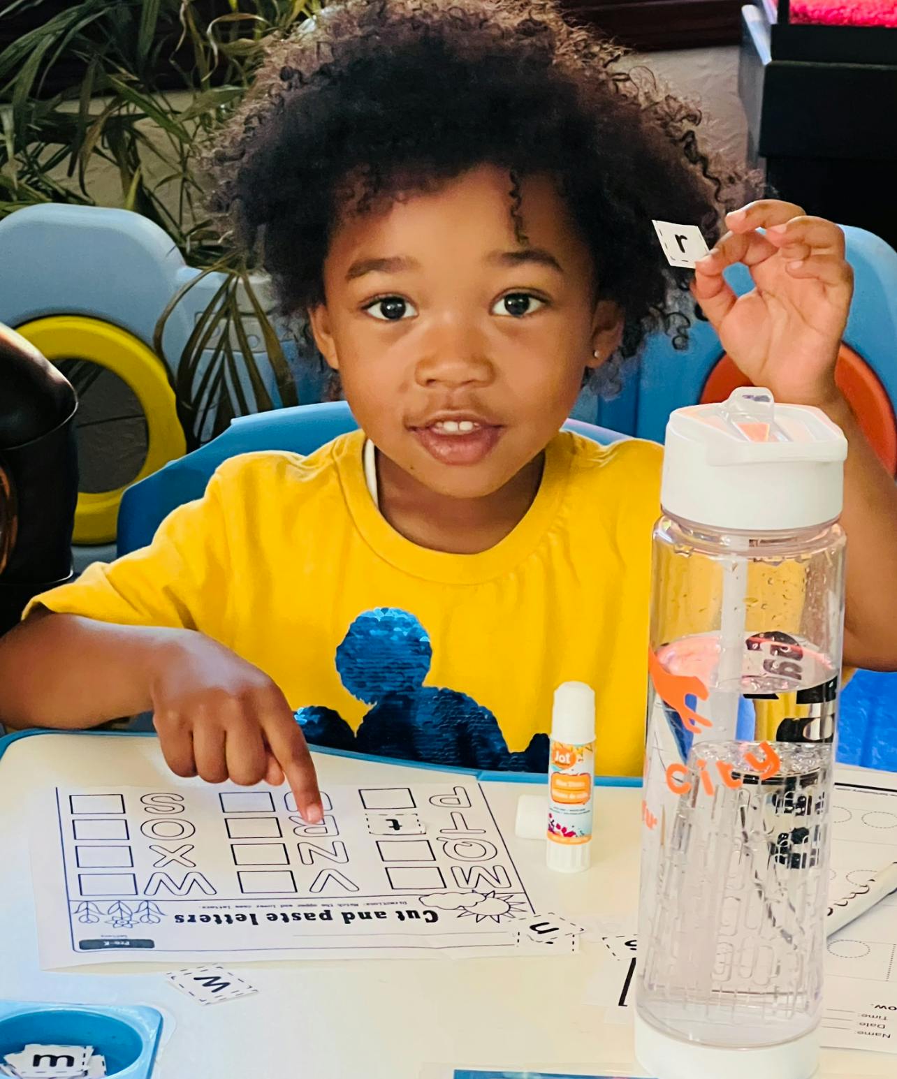 Child holding a letter cutout and pointing at a worksheet