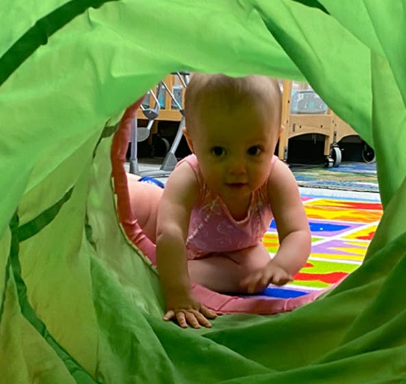Child crawling through a green play tunnel