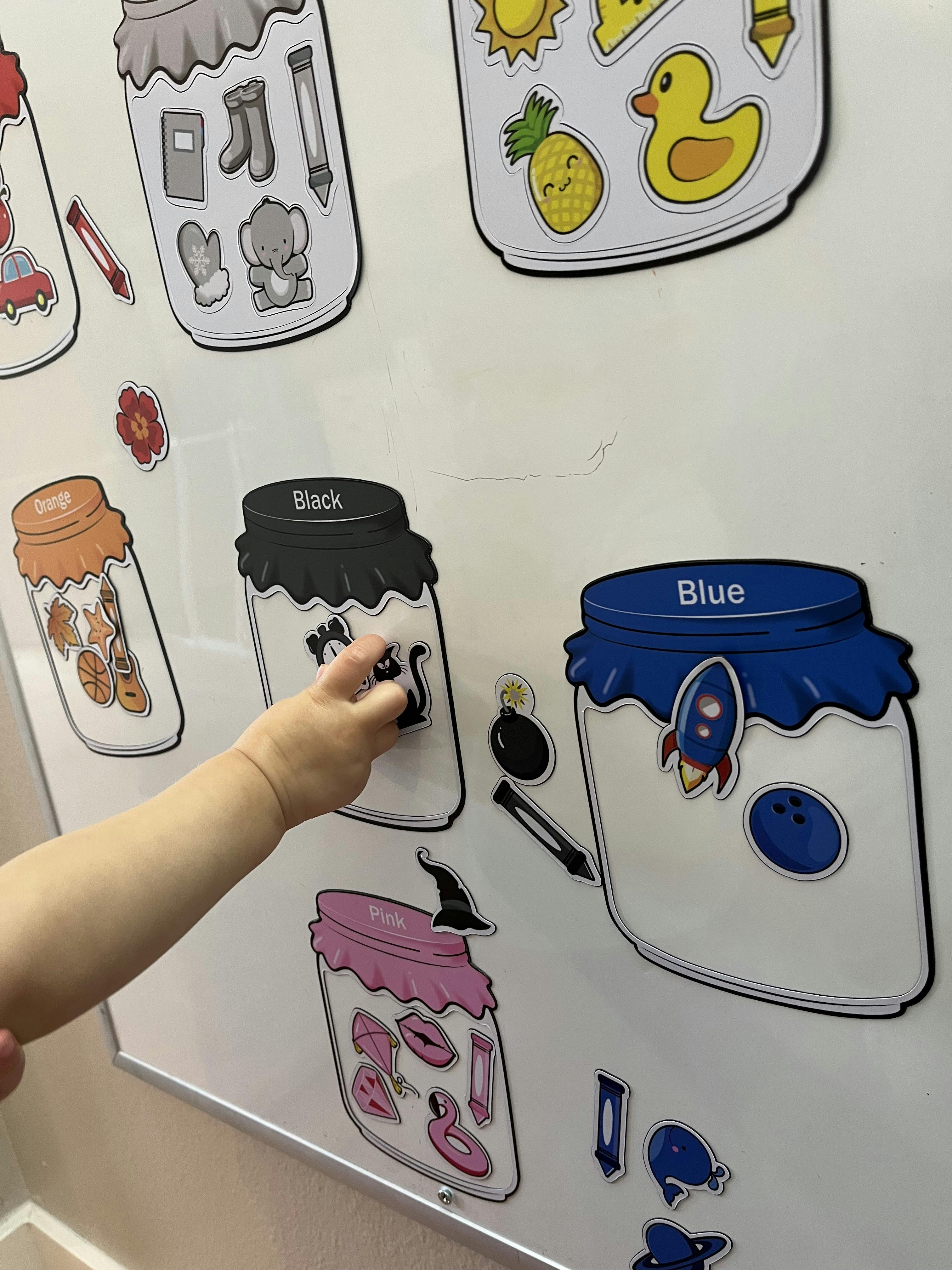 Child's arm placing a black cat magnet on a white board with jar magnets