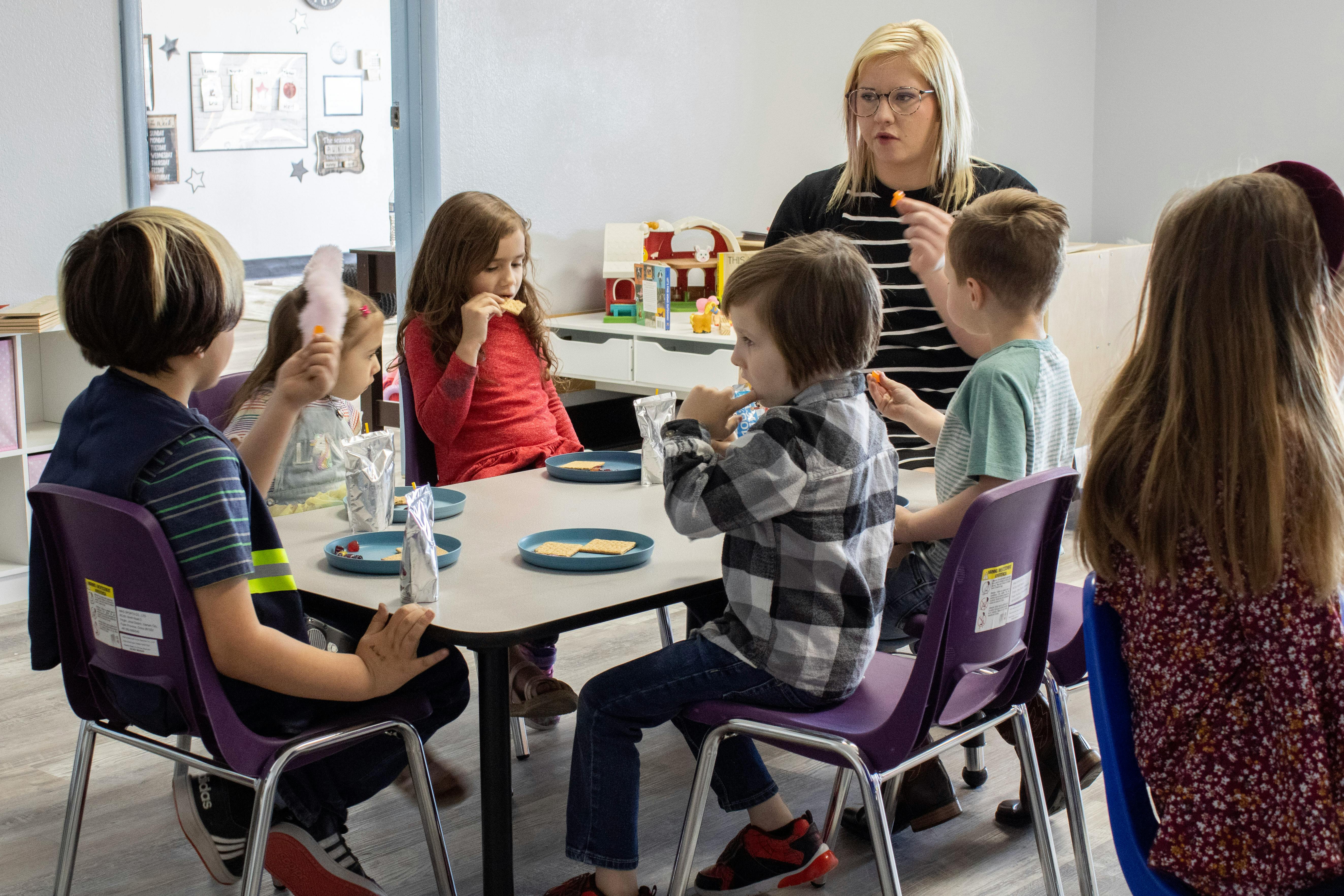 Adult and children sitting at a table eating snacks in a classroom