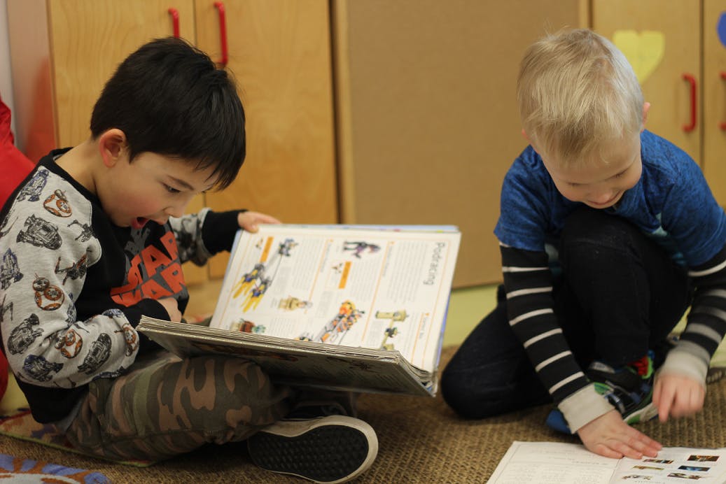 Two children looking at books on the floor