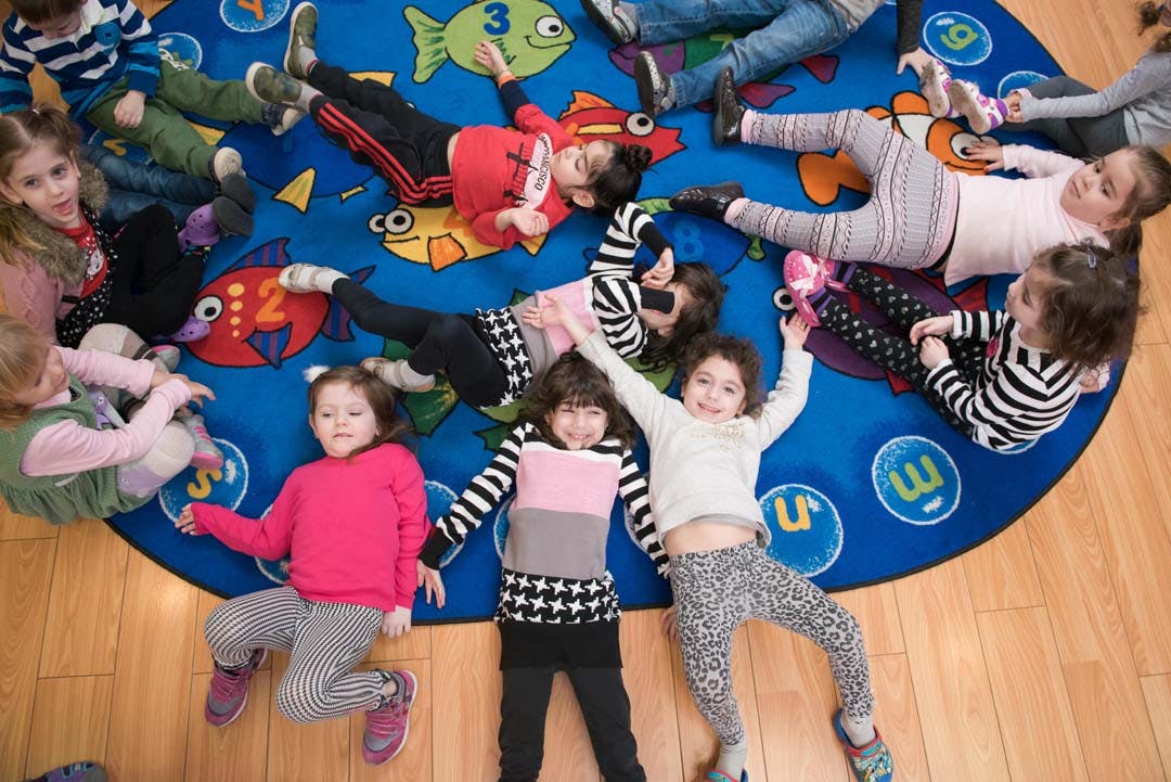 Many children lying on a blue rug with fish designs