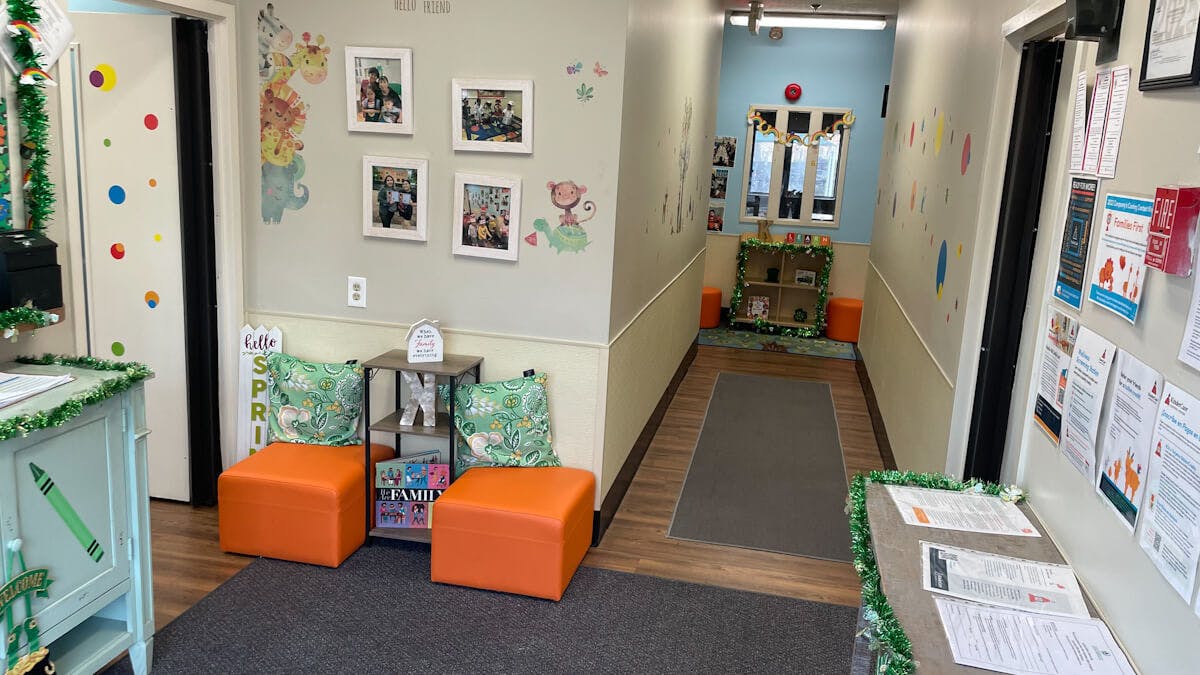 Hallway decorated with children's artwork and photos, orange ottomans, and plants