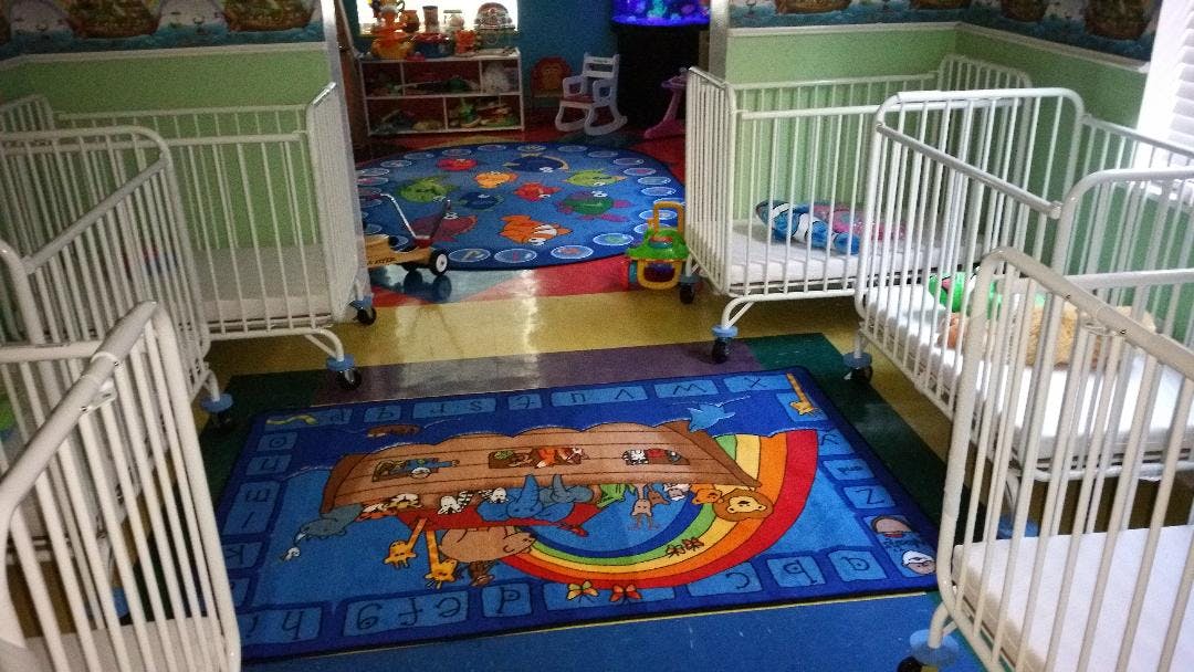 Multiple white cribs in a room with colorful rugs