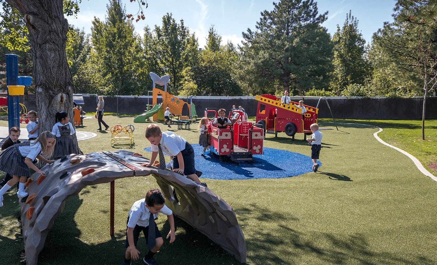 Children playing on a playground with a fire truck structure and climbing logs