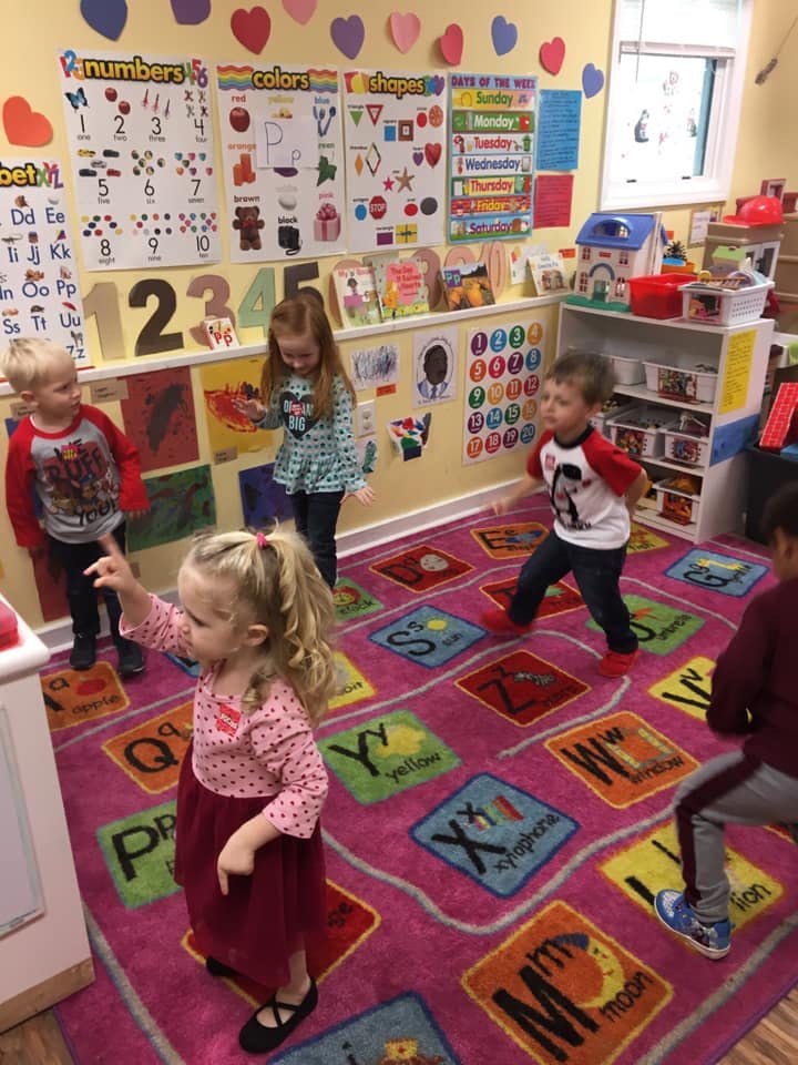 Children playing on a colorful alphabet rug in a classroom