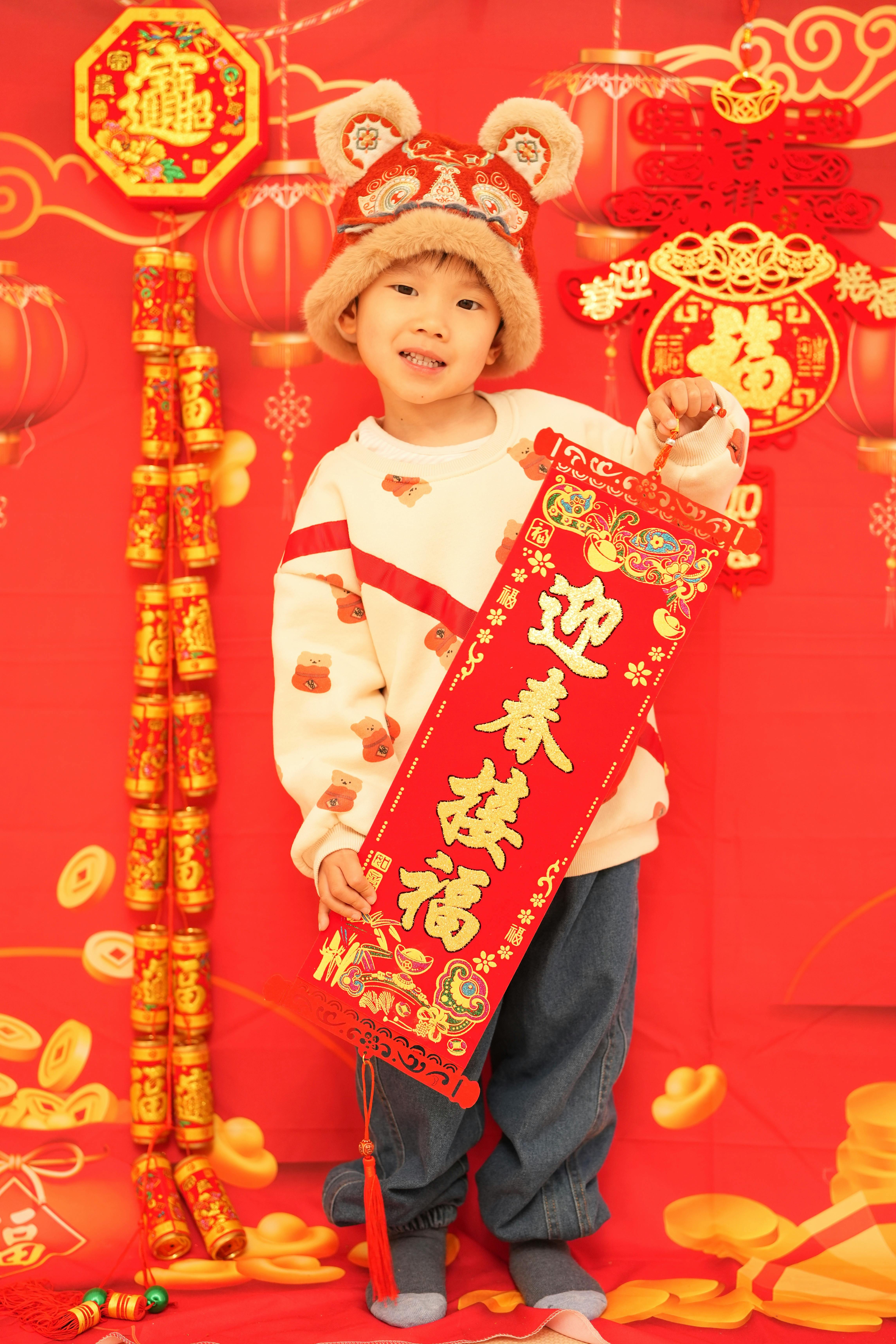 Child wearing a decorative hat holding a red Lunar New Year scroll