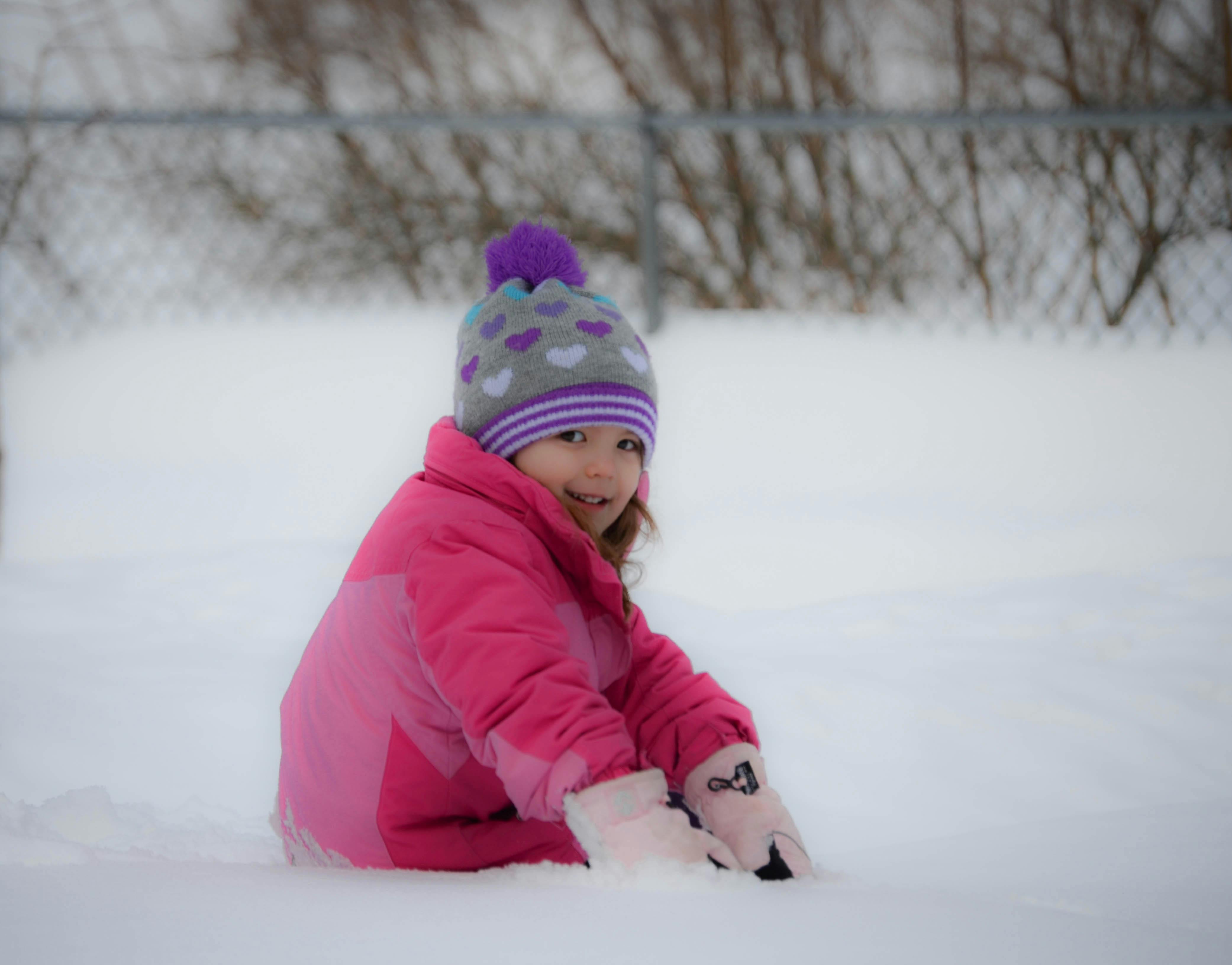 Child in a pink coat and hat sitting in snow