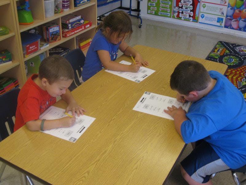 Three children writing at a table in a classroom