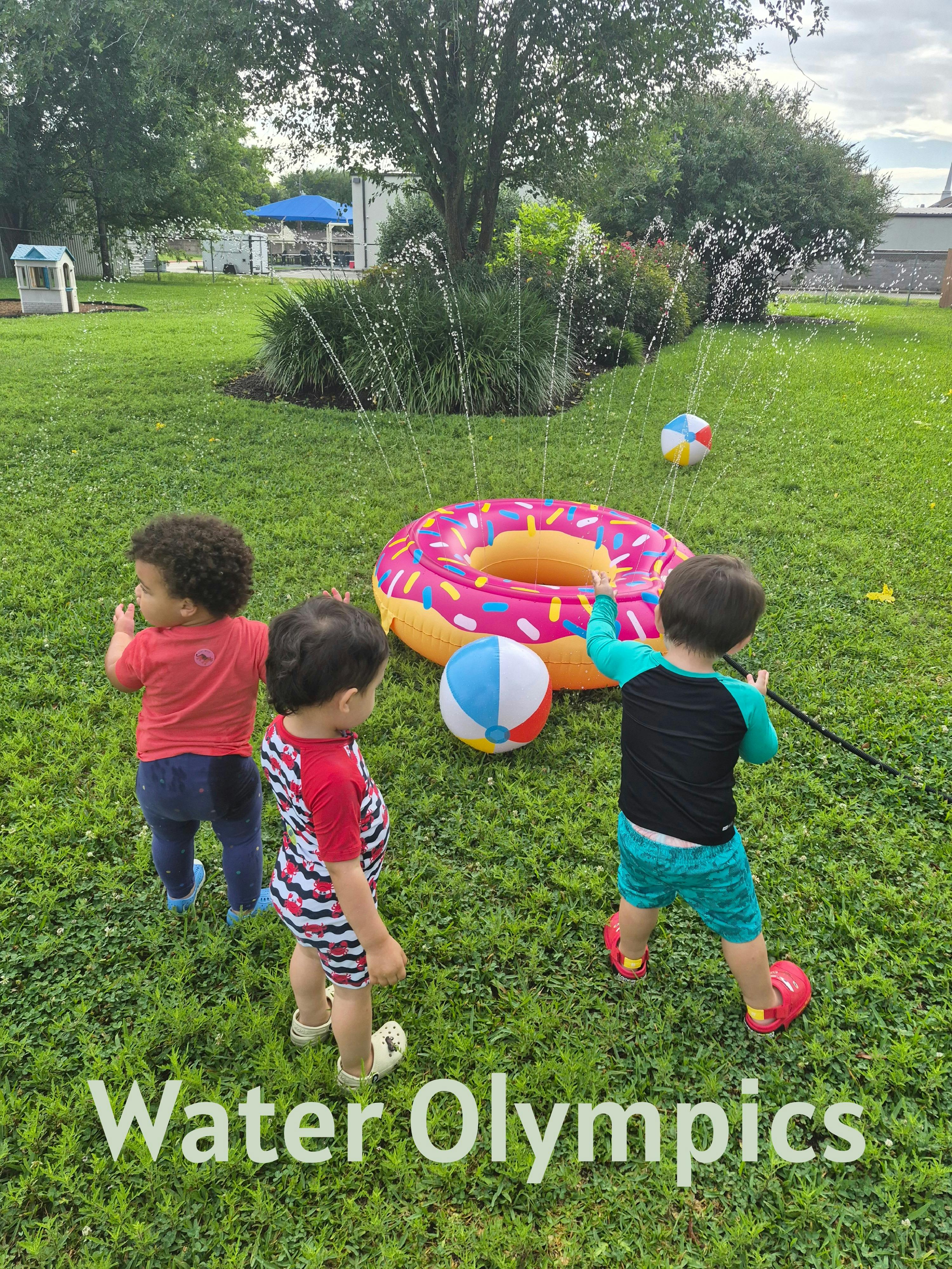 Three children playing with a donut-shaped water sprinkler on a lawn