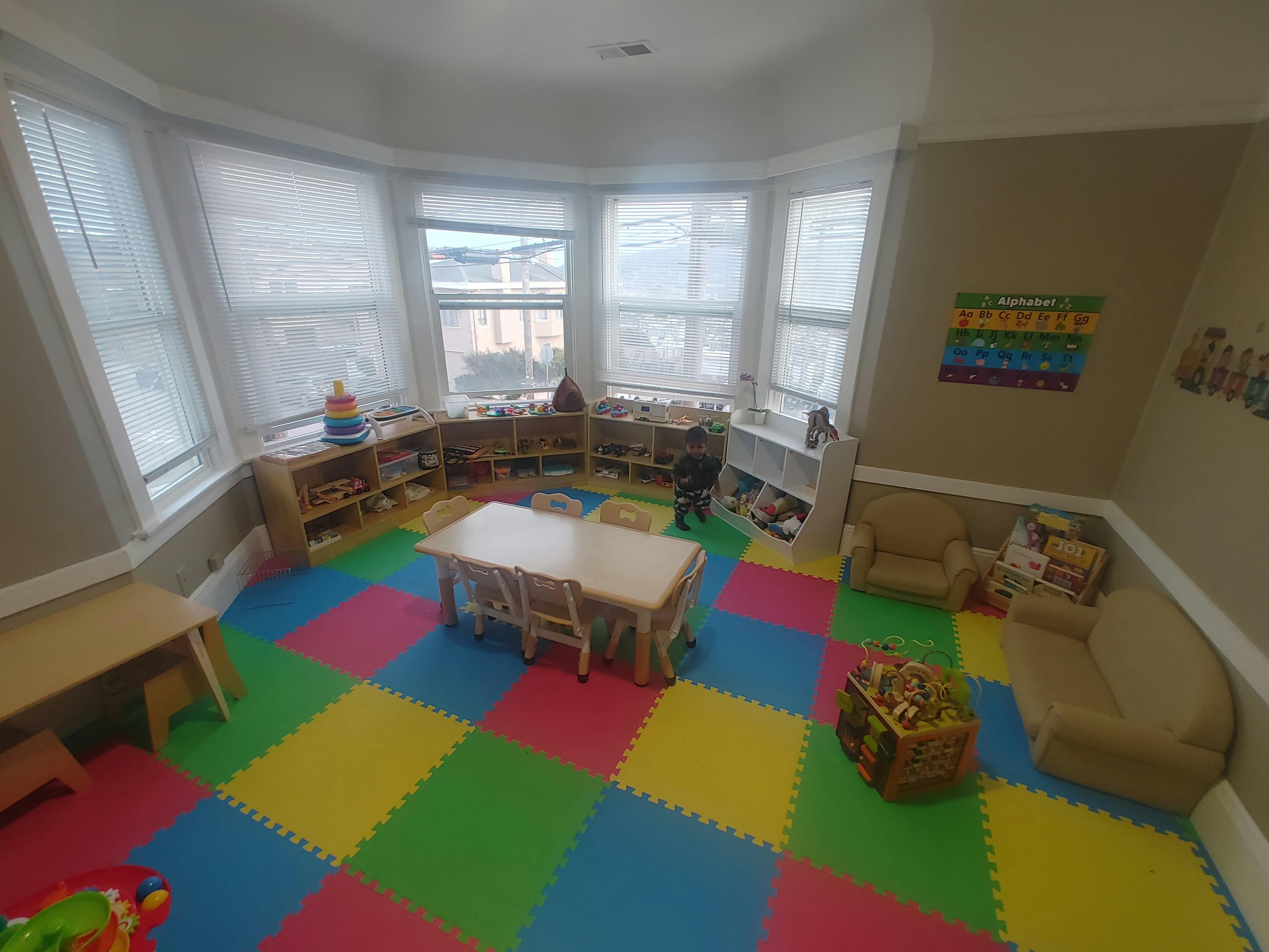 Playroom with colorful floor mats, small tables, chairs, and shelves