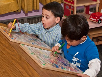 Two children drawing on boards with markers
