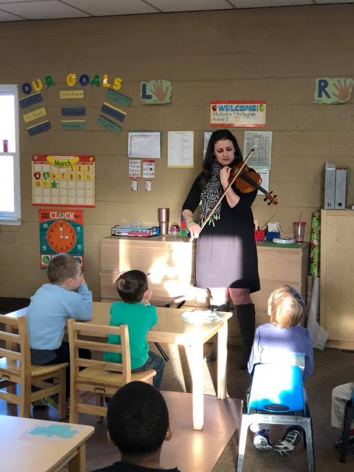 Person playing a violin for children in a classroom