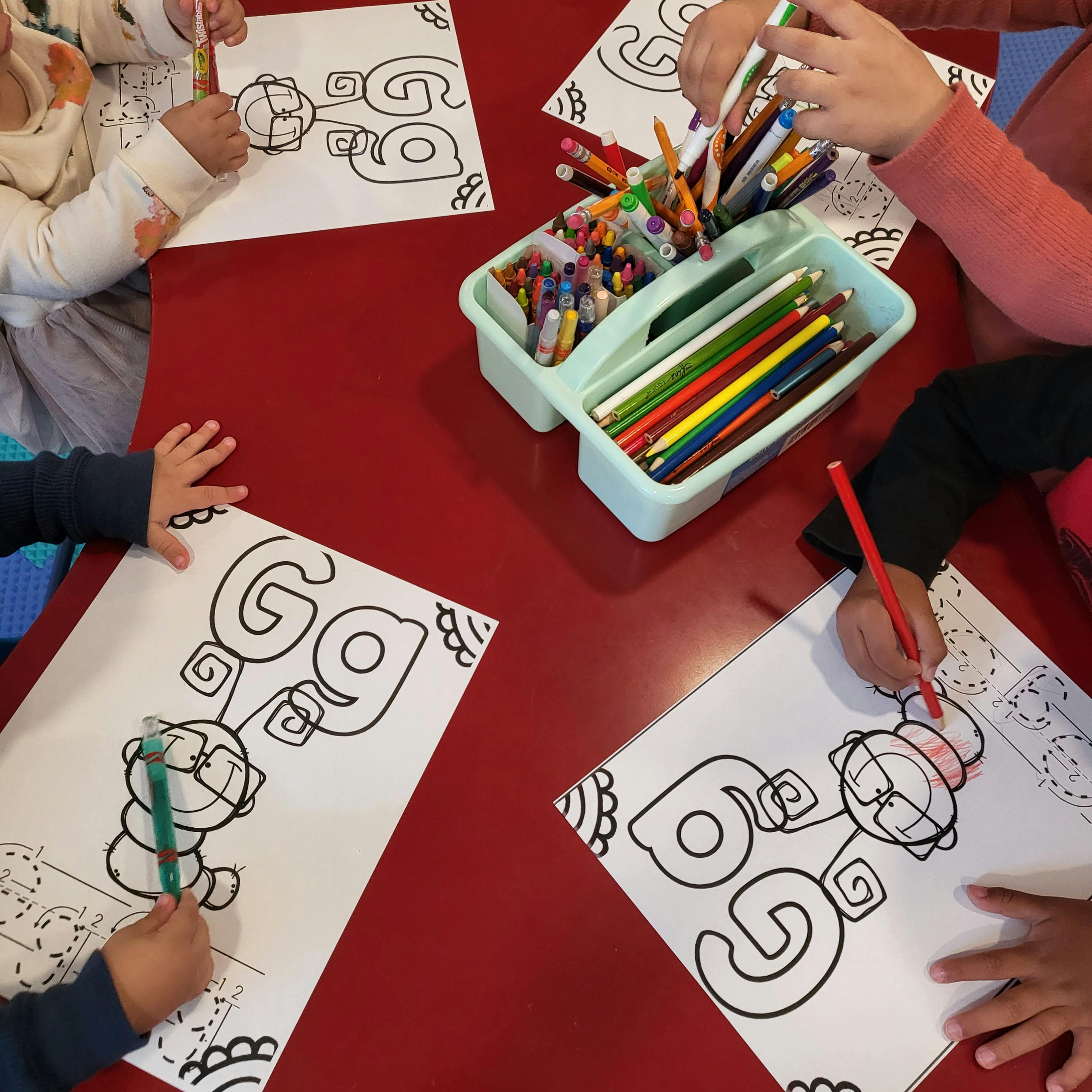 Children coloring Gg letter worksheets at a table