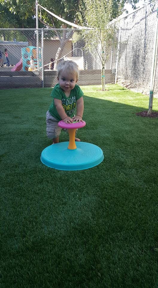 Child standing on grass with hands on a colorful spinning toy