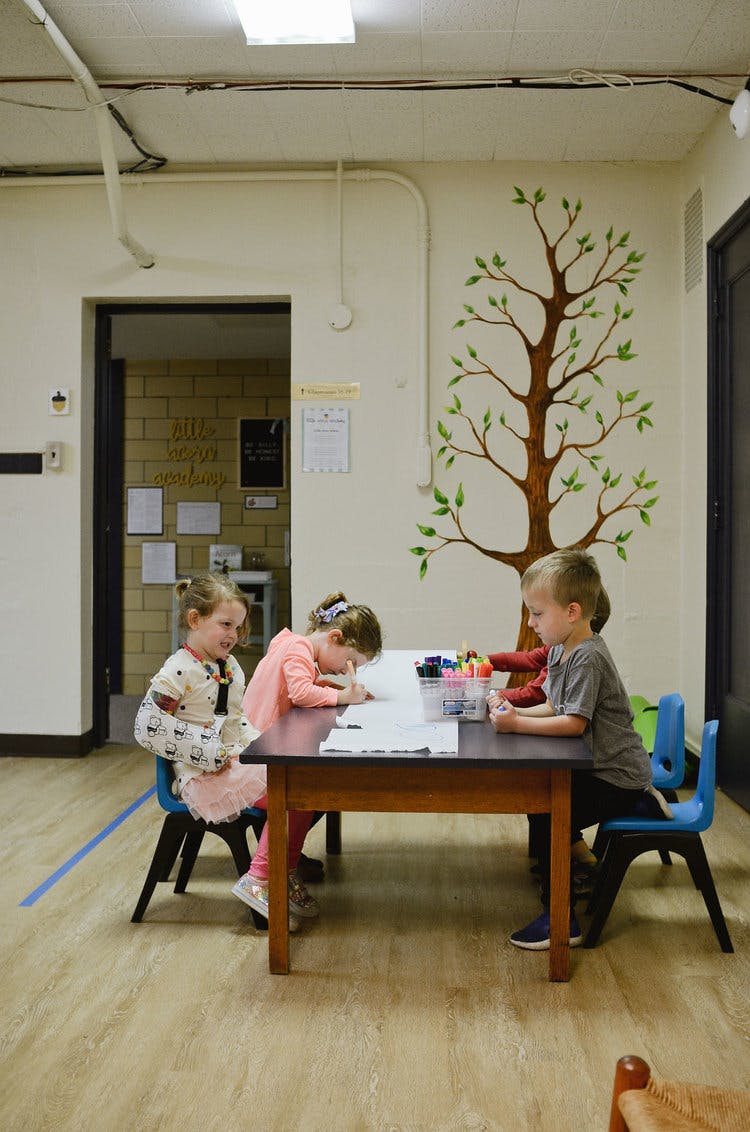 Three children drawing at a table in a classroom