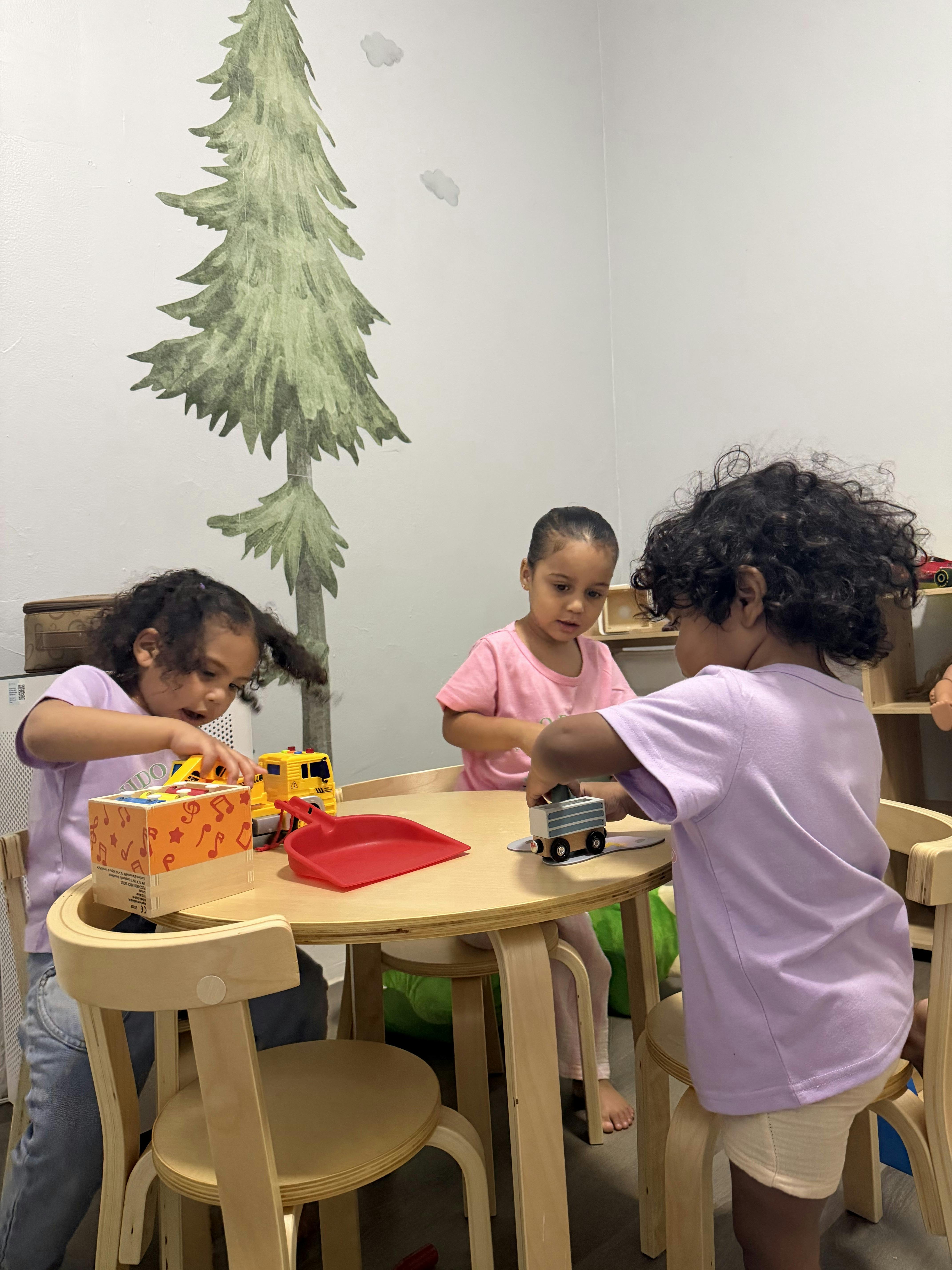 Three children playing with toys at a small wooden table