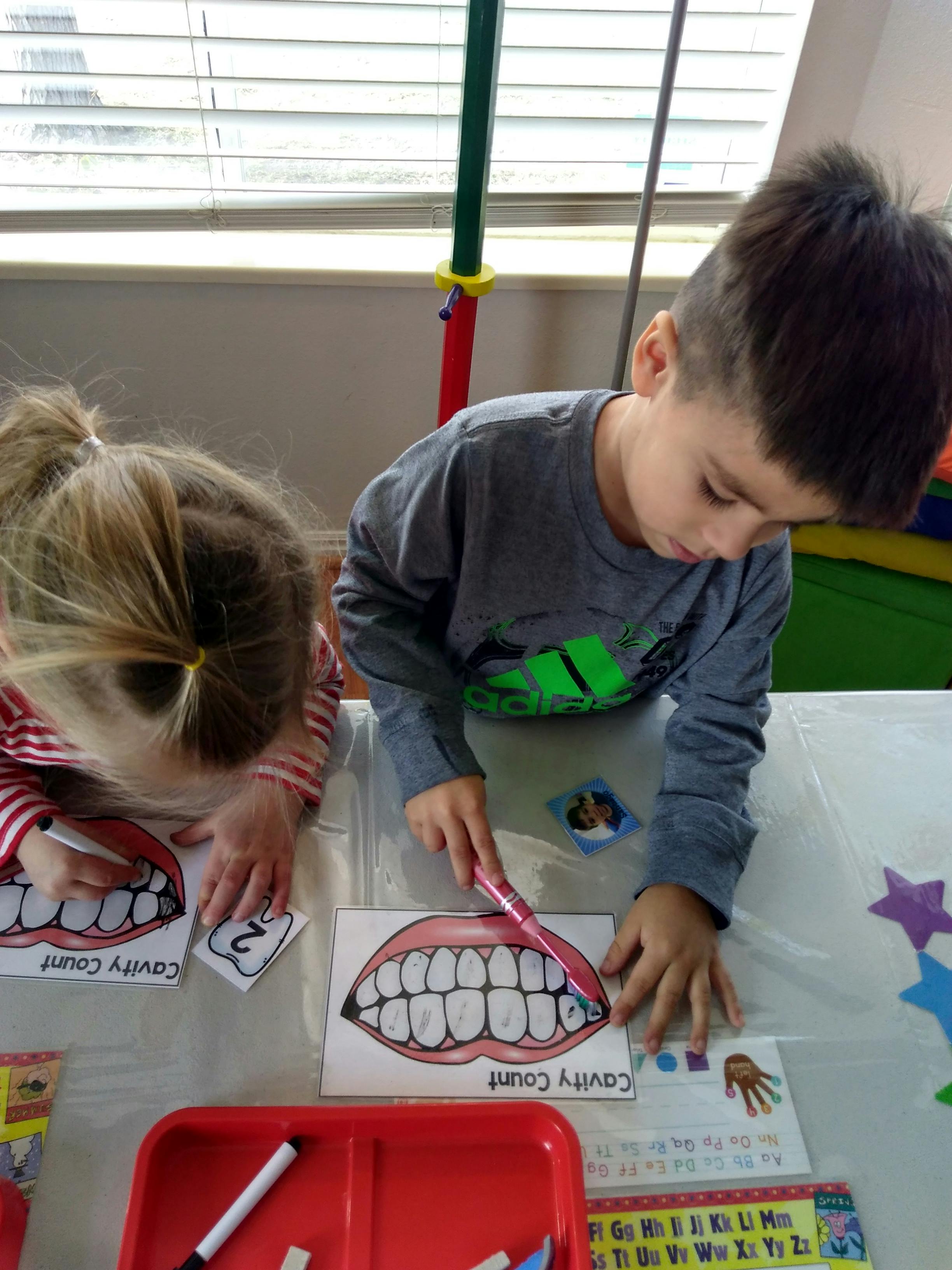 Two children doing a dental health activity with toothbrushes and teeth diagrams