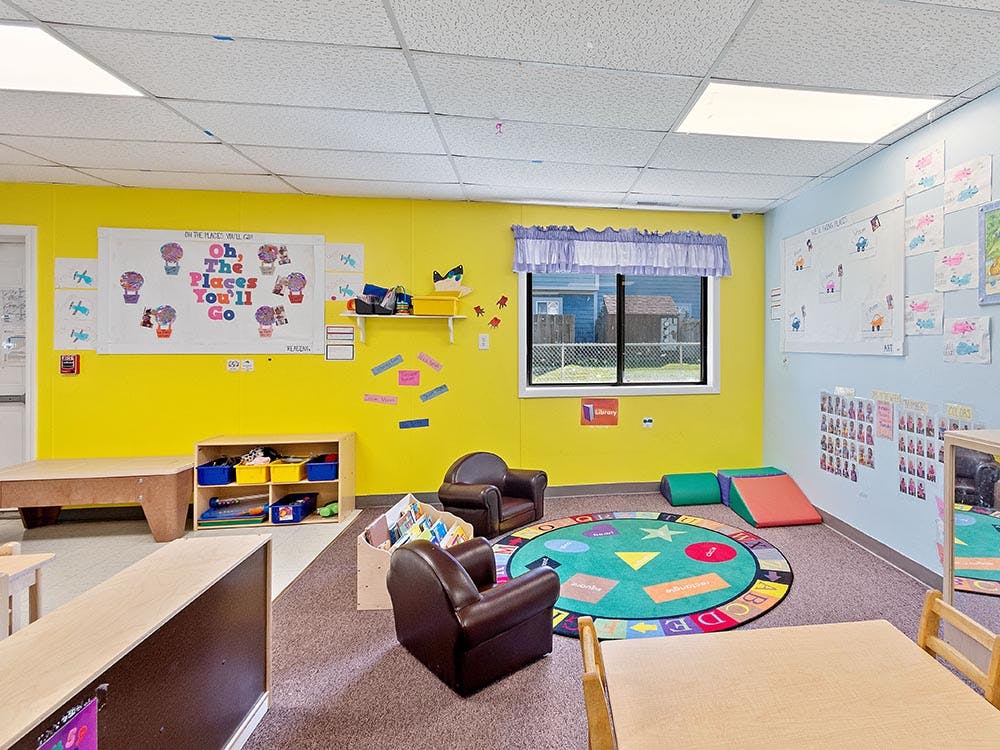 A classroom with a yellow wall, window, and a reading nook