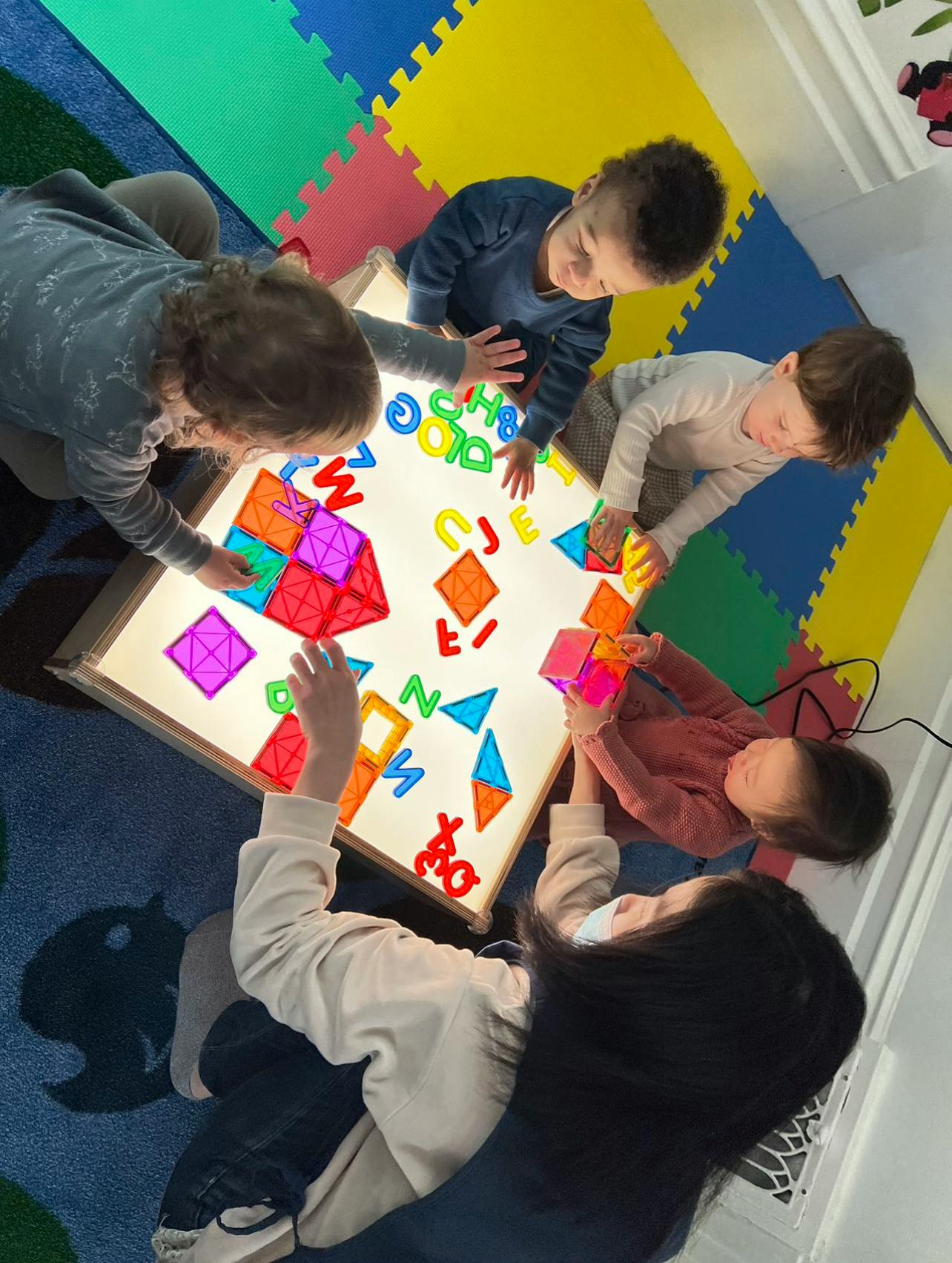 Children playing with colorful shapes and letters on a light table