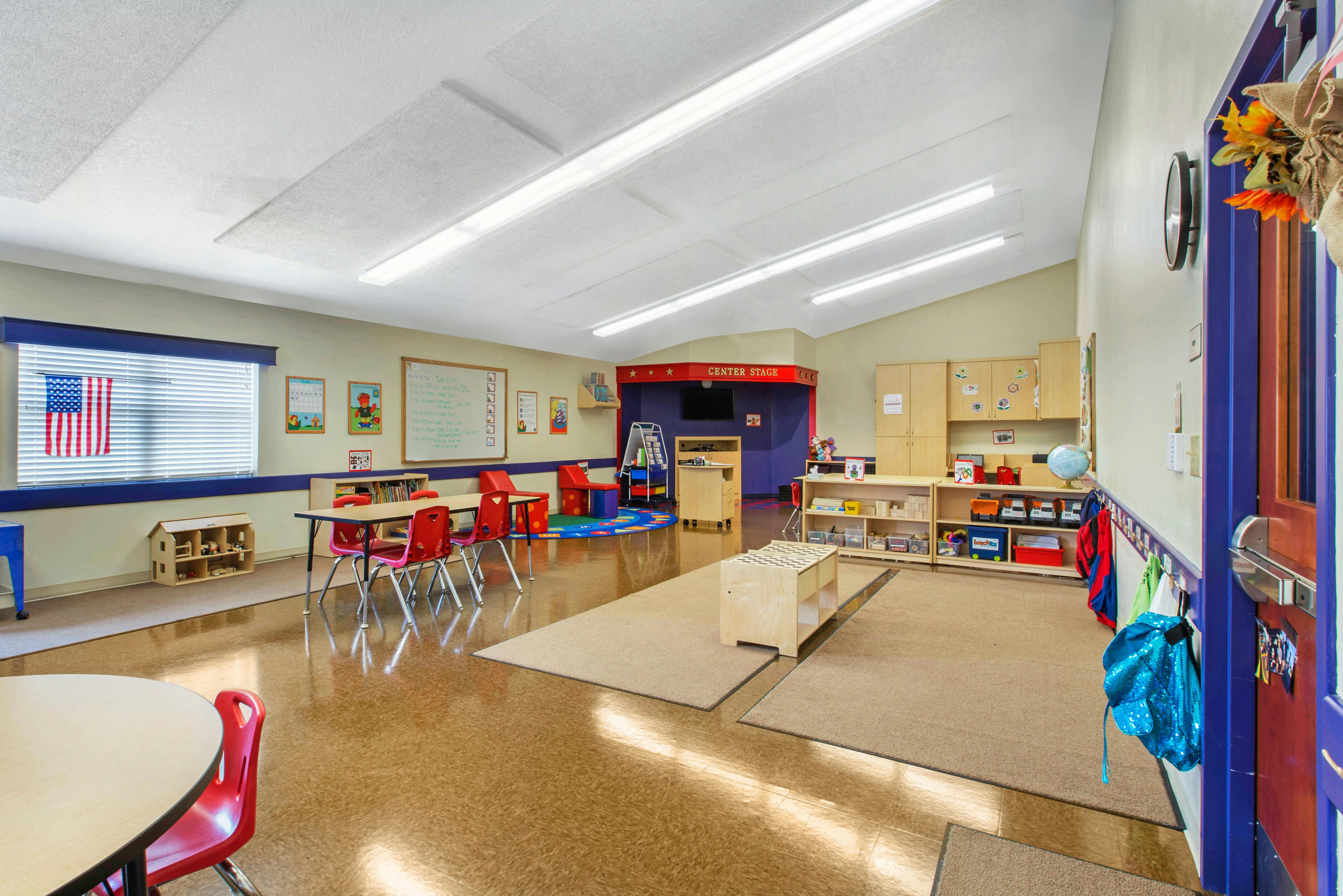 Classroom with tables and chairs, play area, and storage shelves