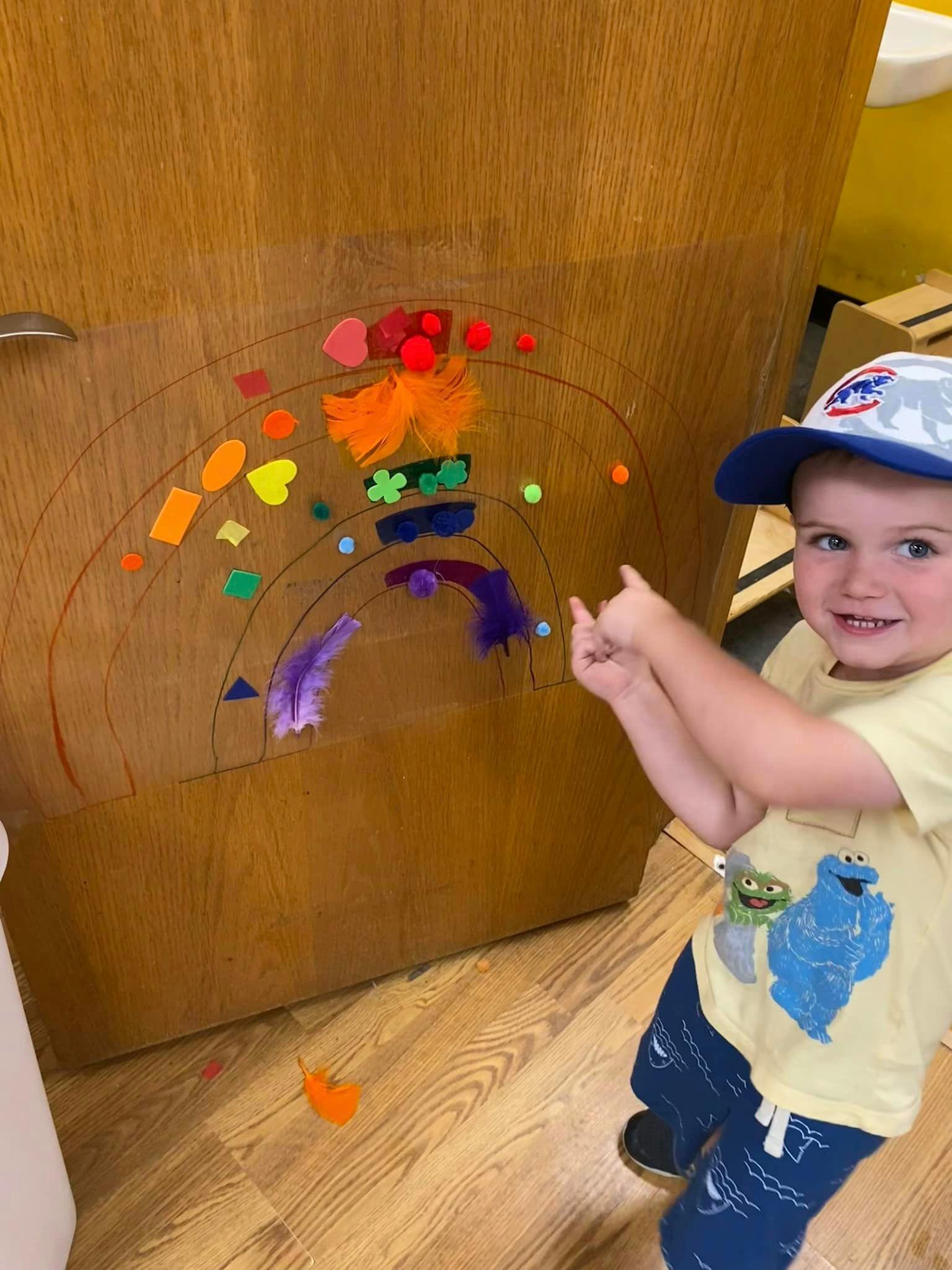 Child pointing at a rainbow craft on a wooden surface