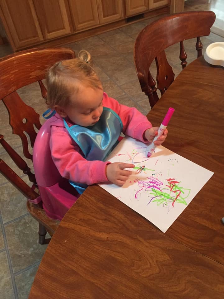 Child in a high chair drawing on paper with a marker