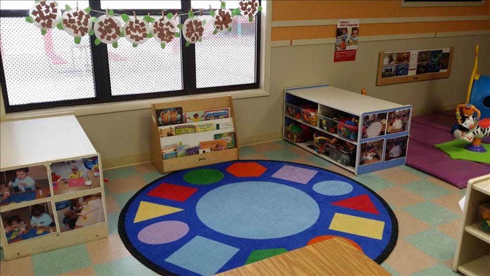 Classroom with child-sized furniture, colorful rug, and windows with decorations