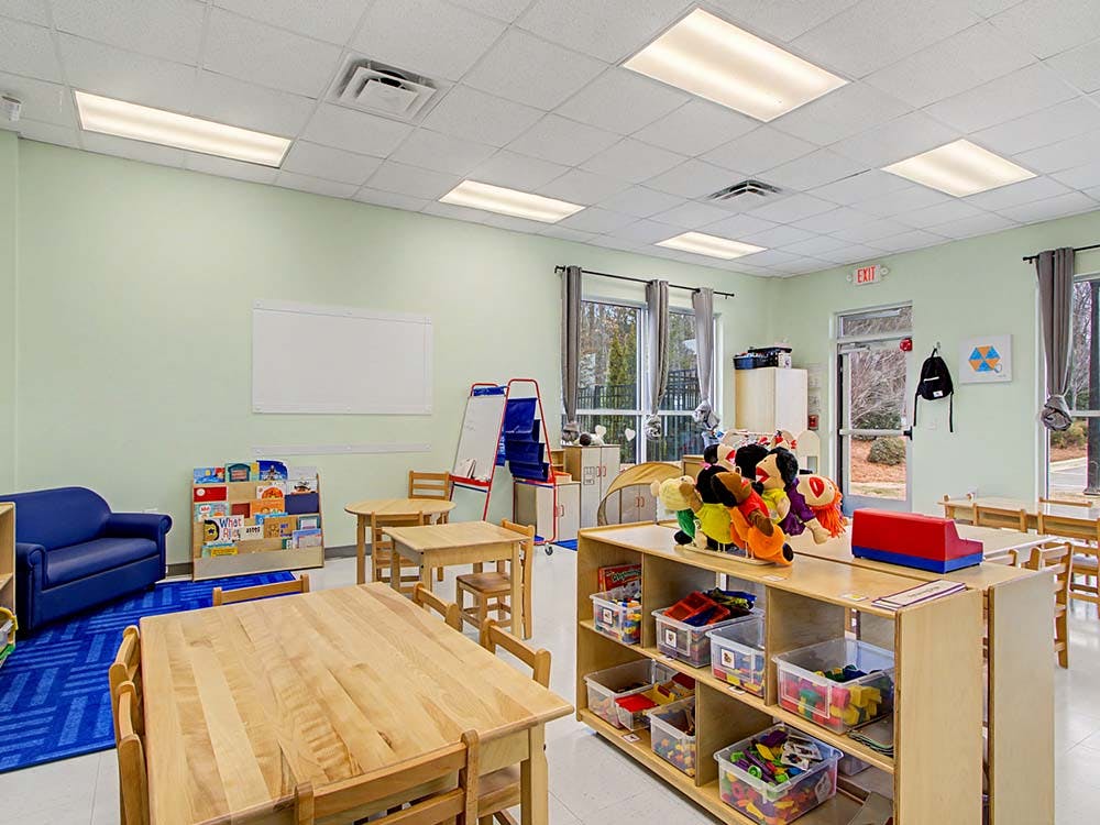 Classroom with small wooden tables and chairs, a blue sofa, and toy storage