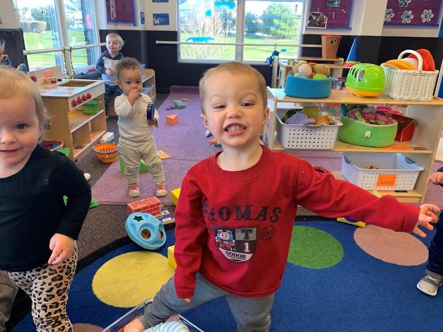 Three children in a classroom, one child in a red shirt smiling at the front