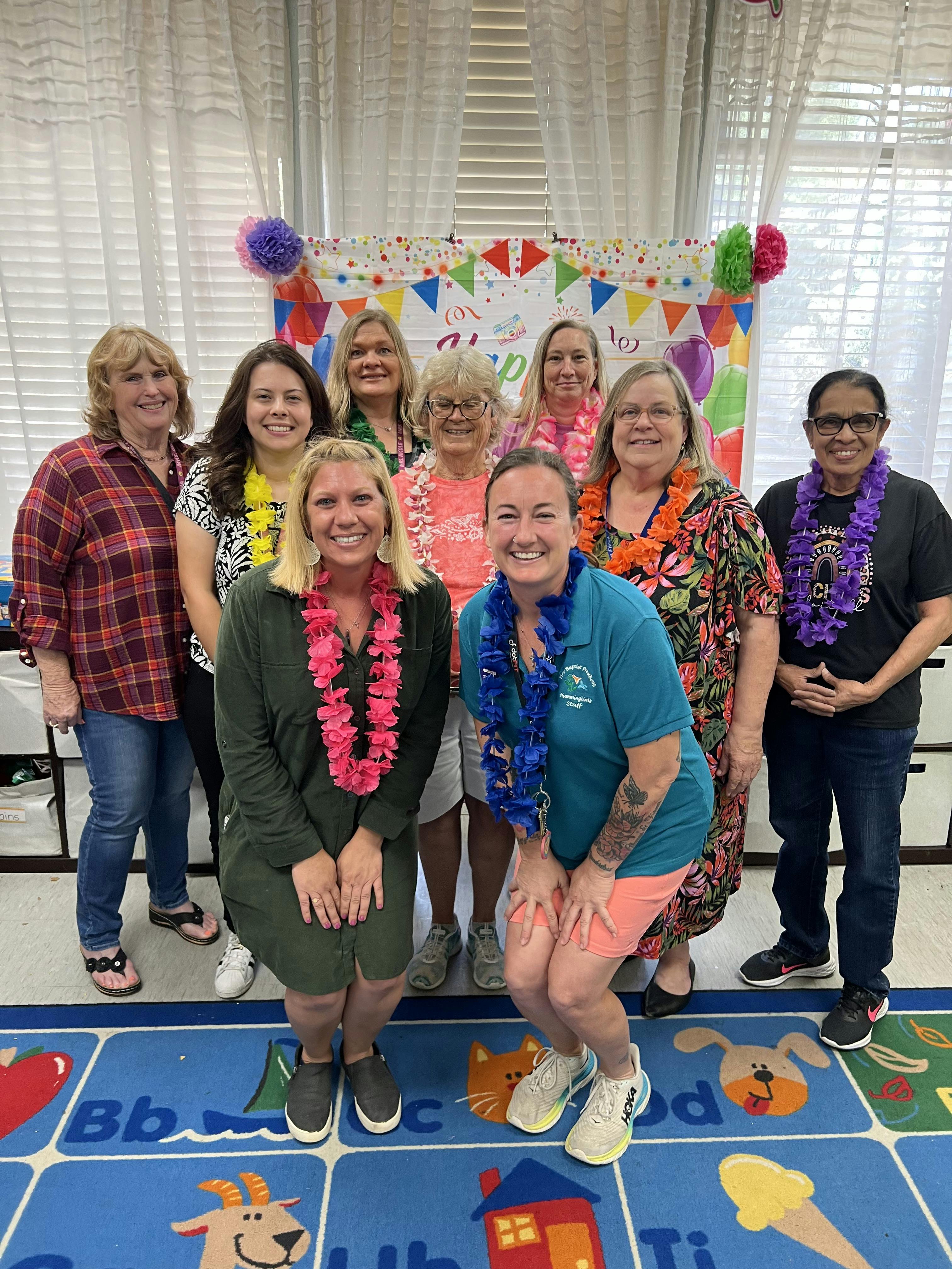 Group of people wearing leis standing in front of a colorful banner