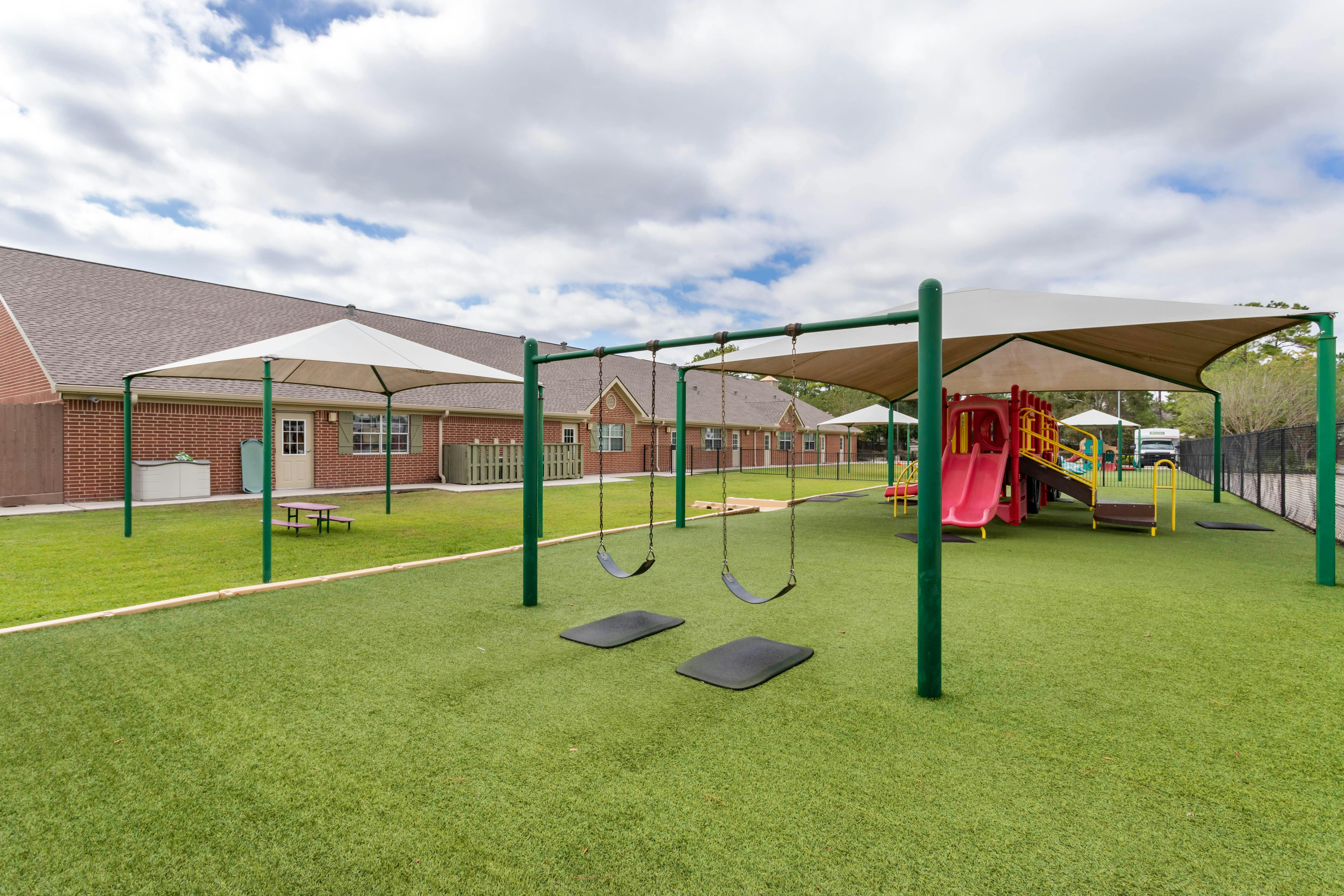 Playground with swings, slides, artificial turf, and shaded areas