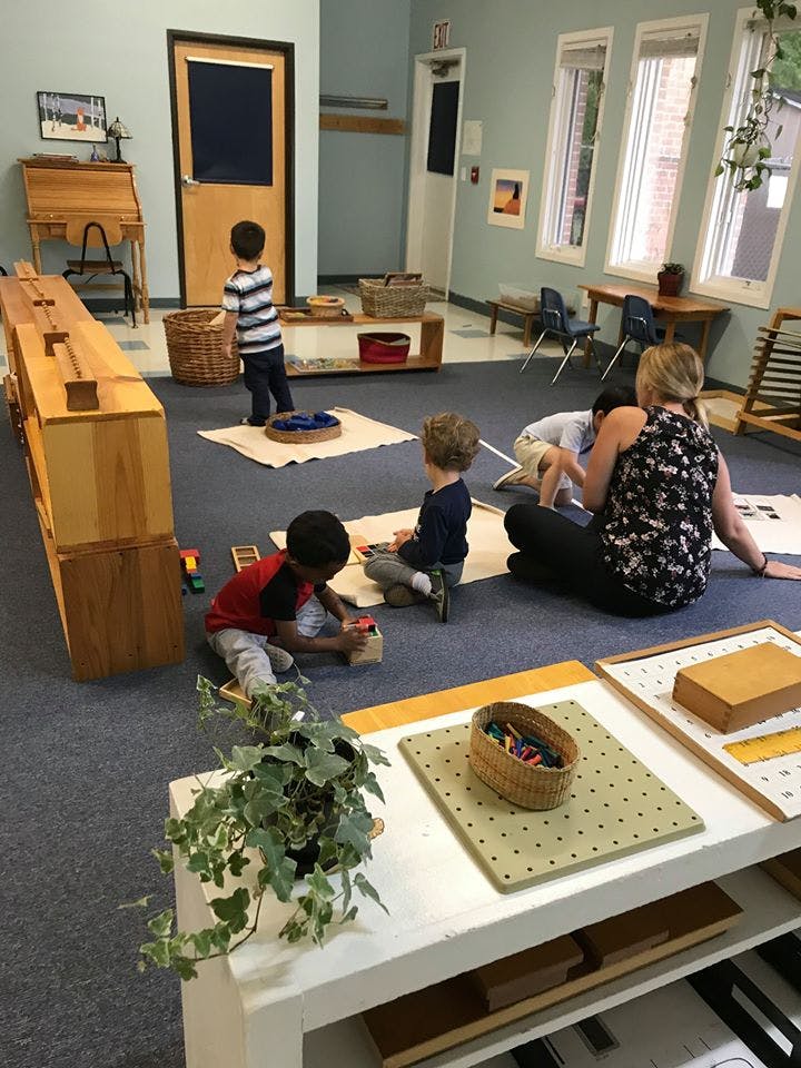 Adult and children playing with toys on the floor in a classroom