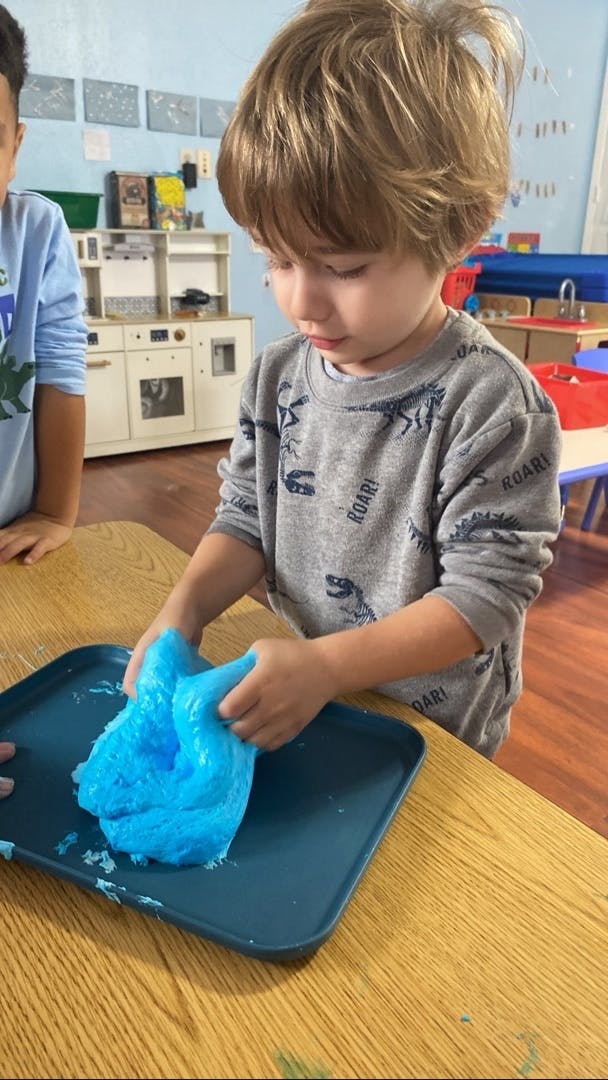 Child playing with blue slime on a blue tray