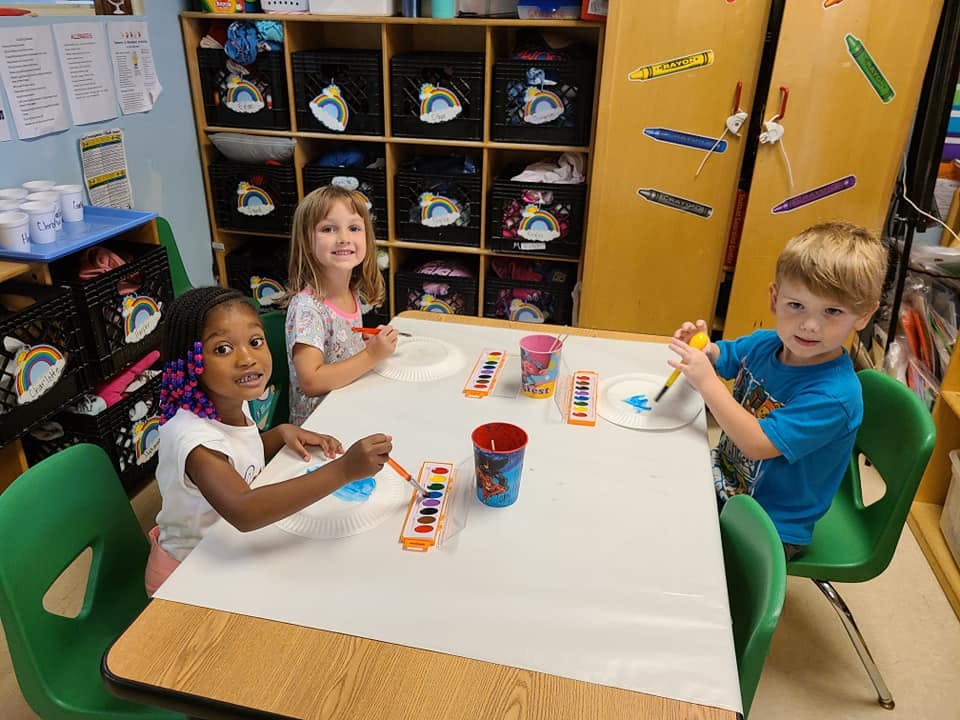 Three children painting at a table in a classroom