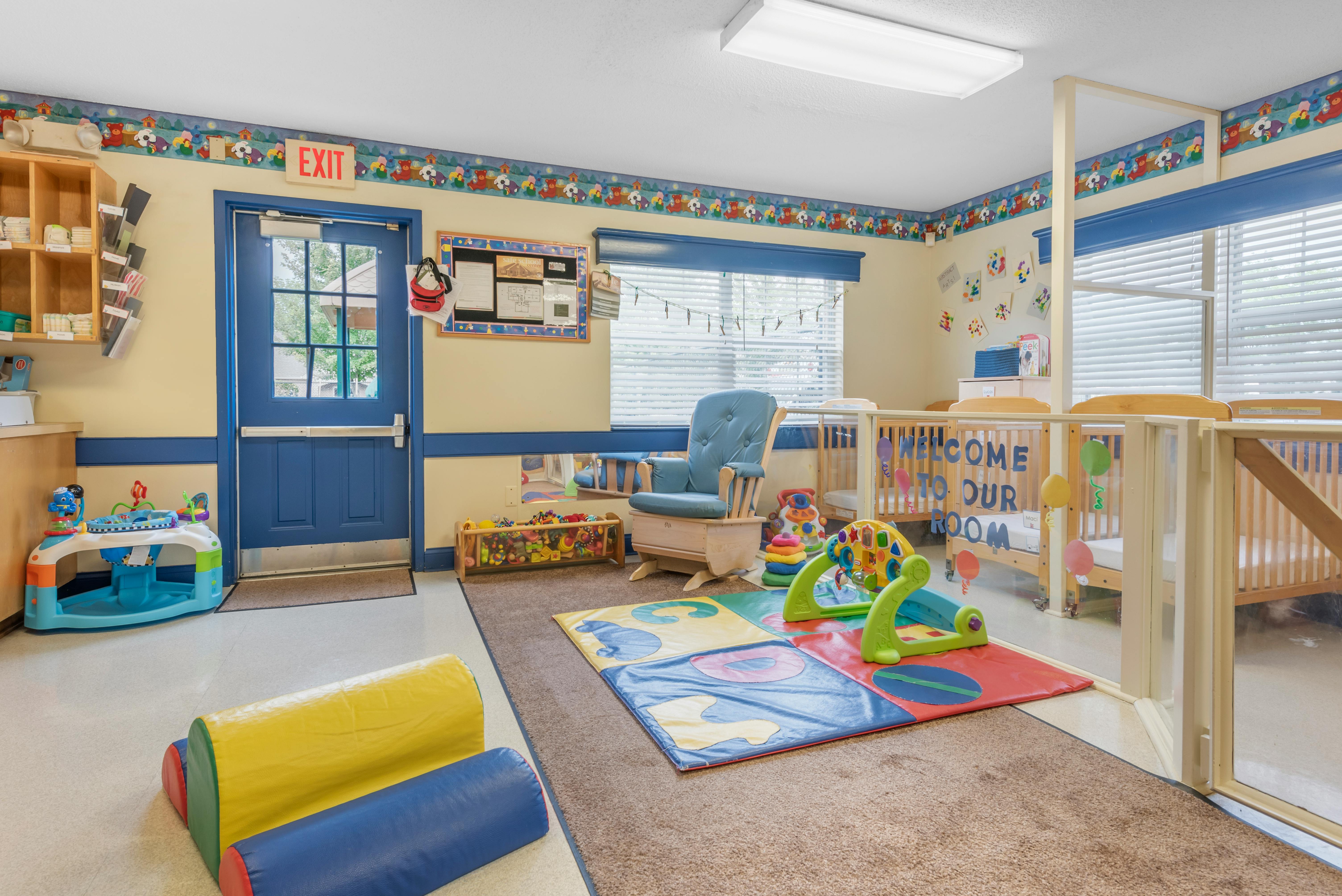 Baby nursery with cribs, play mat, rocking chair, and an exit sign above a door