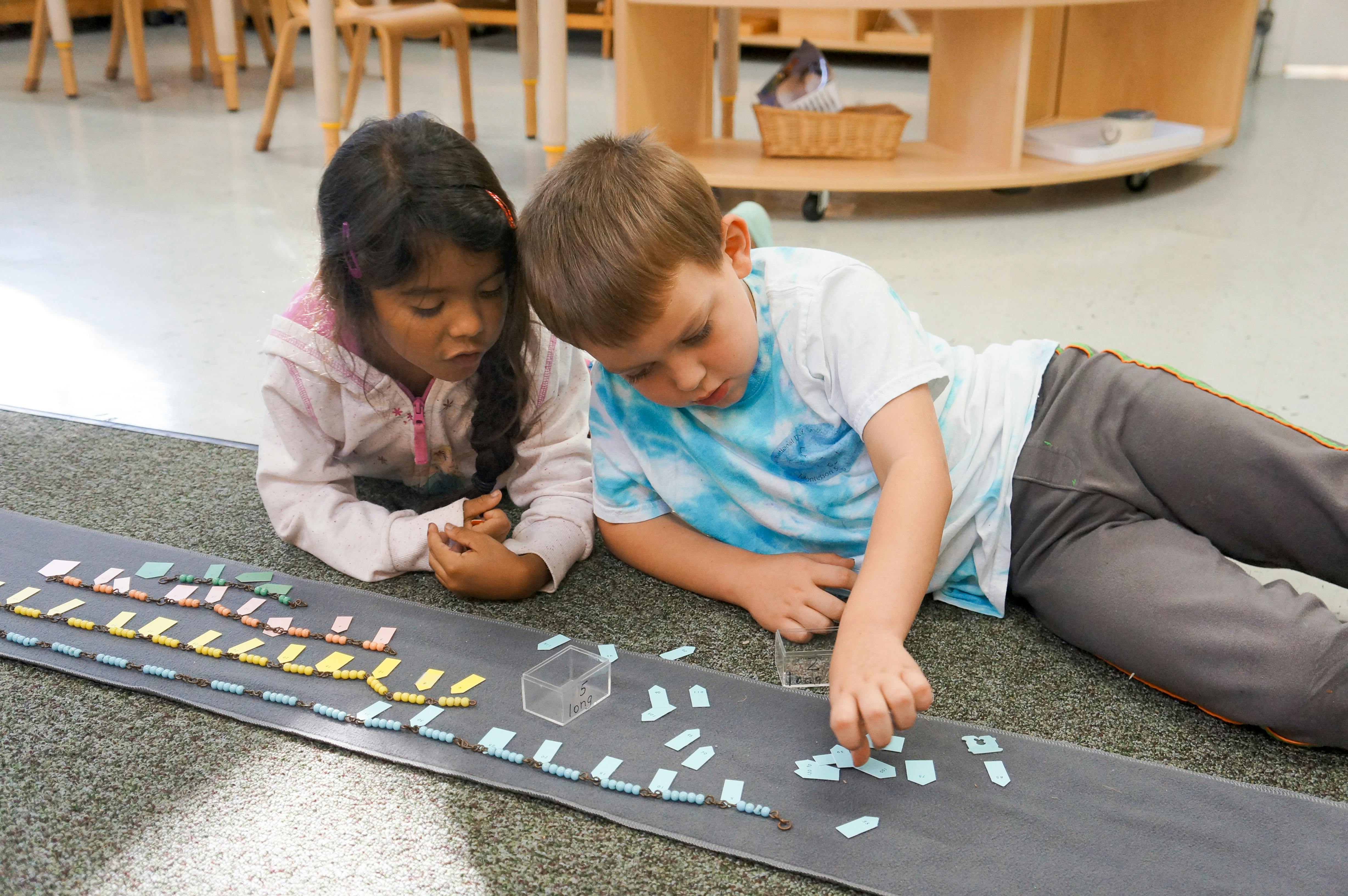 Two children lying on the floor playing with small blocks