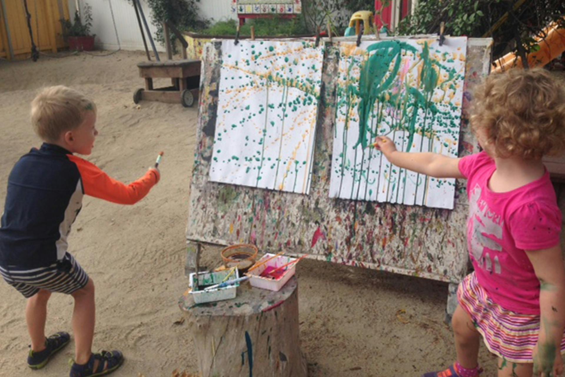 Two children painting on an easel outdoors