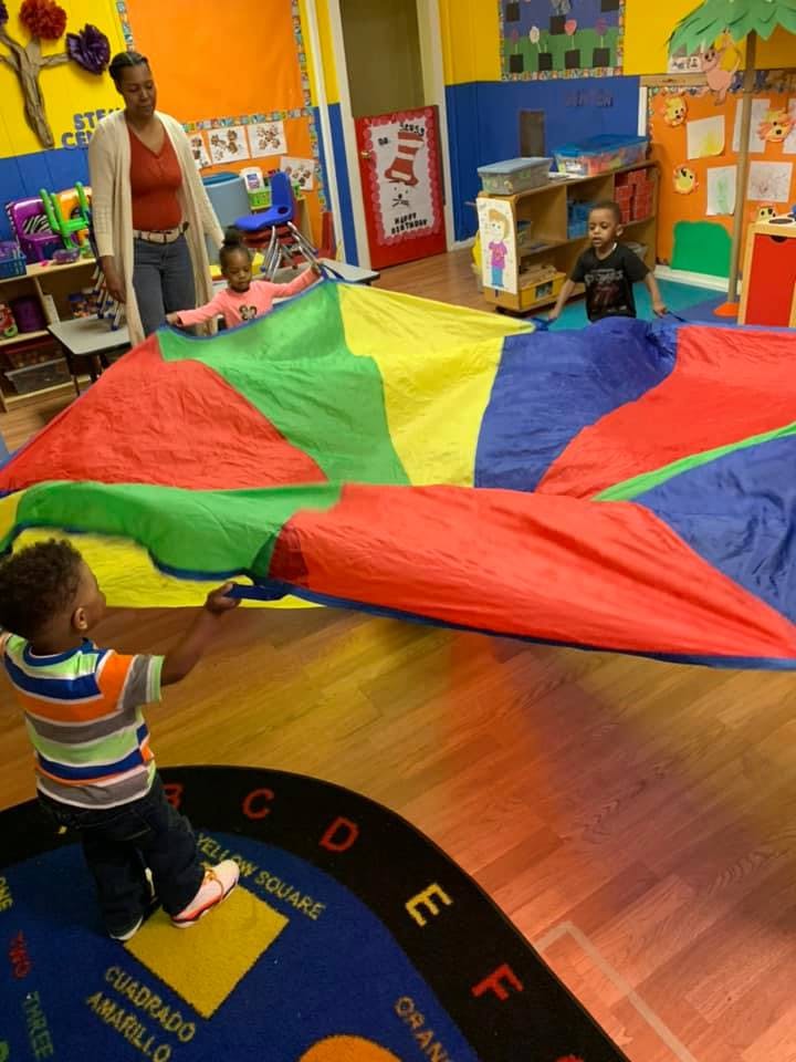 Adult and children playing with a colorful parachute in a classroom