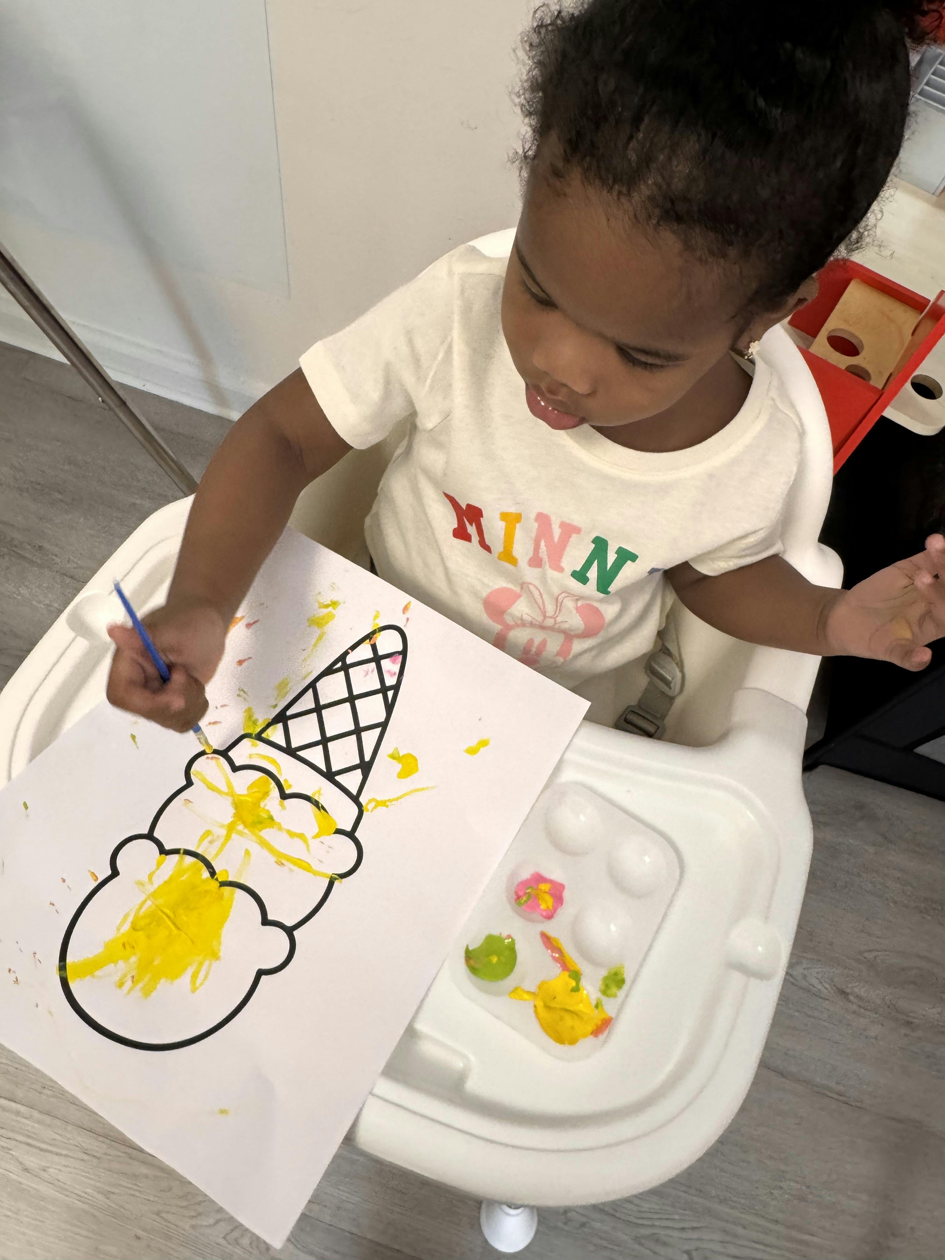 Child sitting in a high chair painting an ice cream drawing