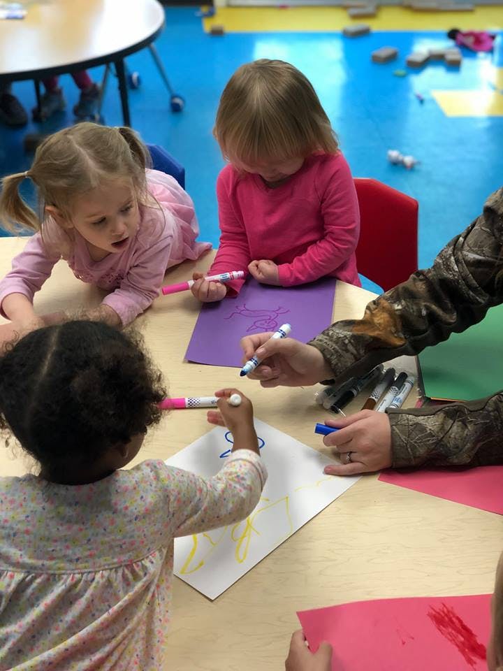 Children and an adult drawing with markers at a table