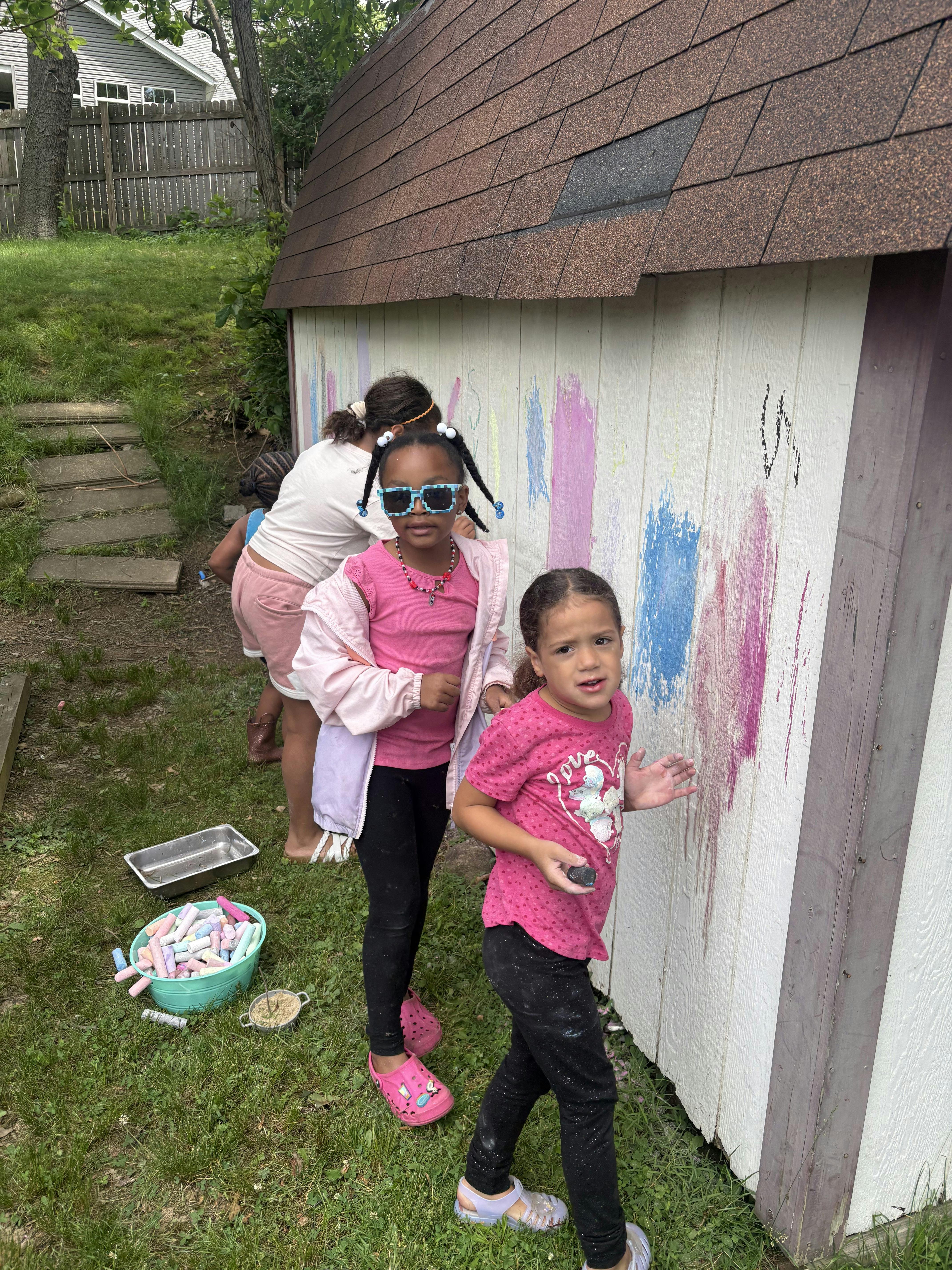 Children drawing with chalk on the side of a shed