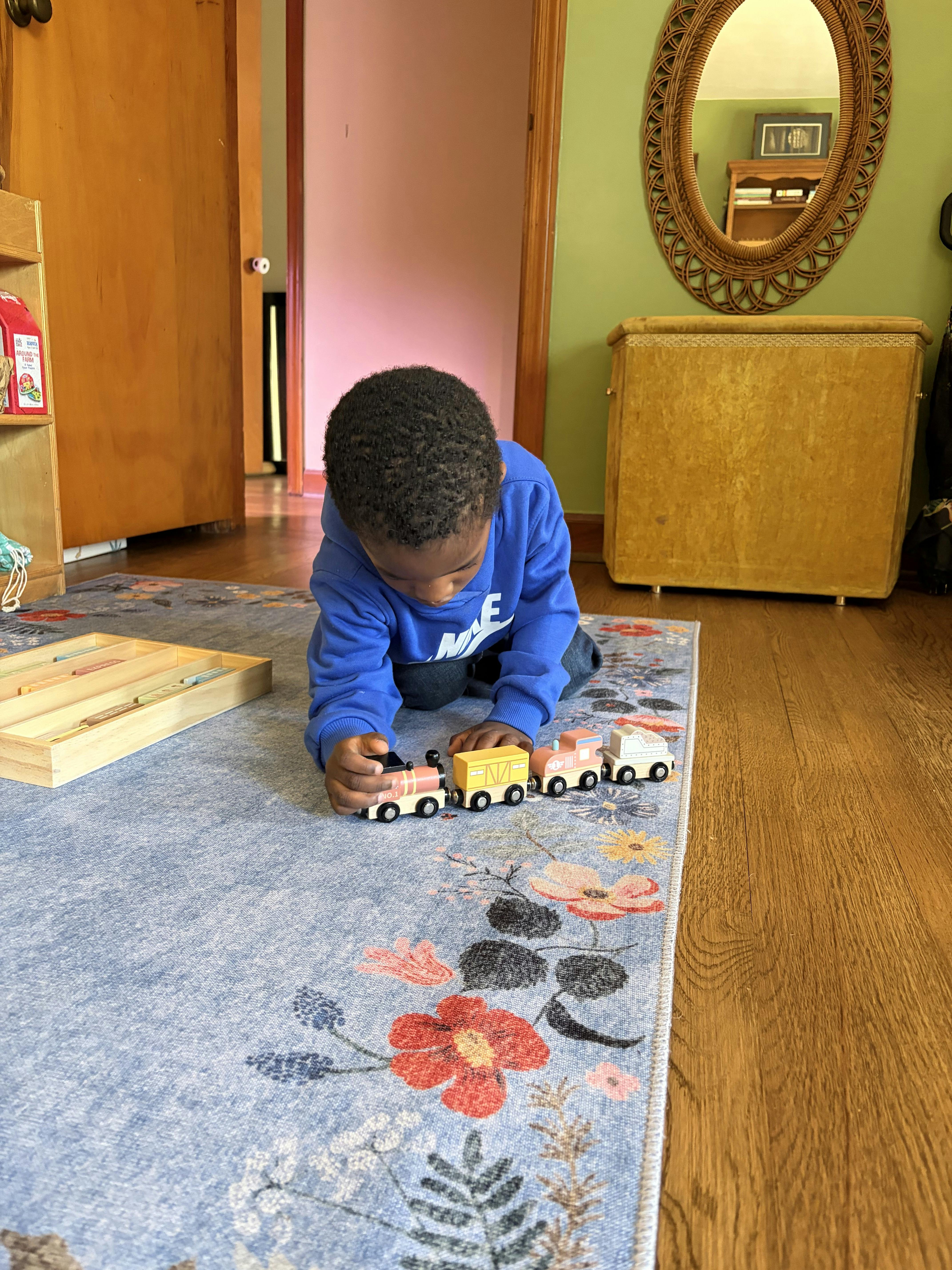 Child playing with a wooden toy train on a floral area rug