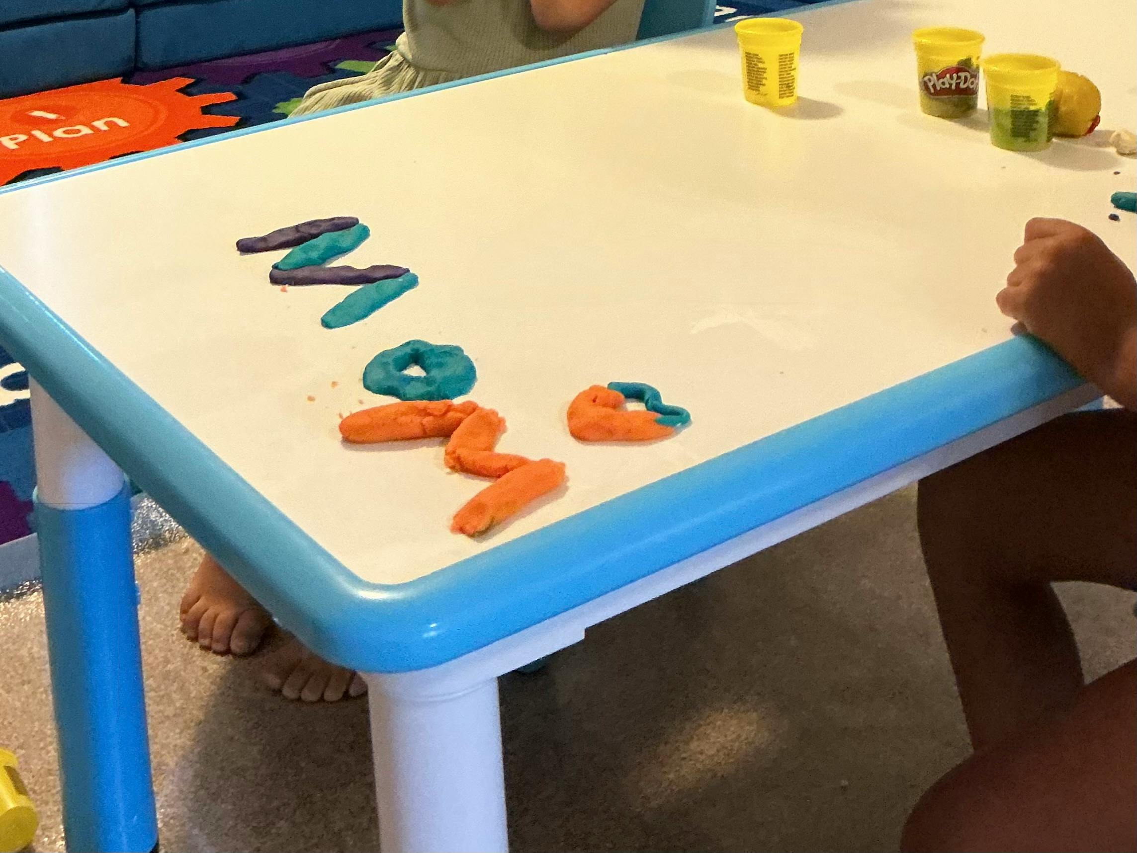 Child crafting the word mom with playdough on a table