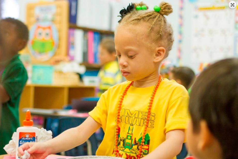 Child in a yellow shirt with beads using glue in a classroom