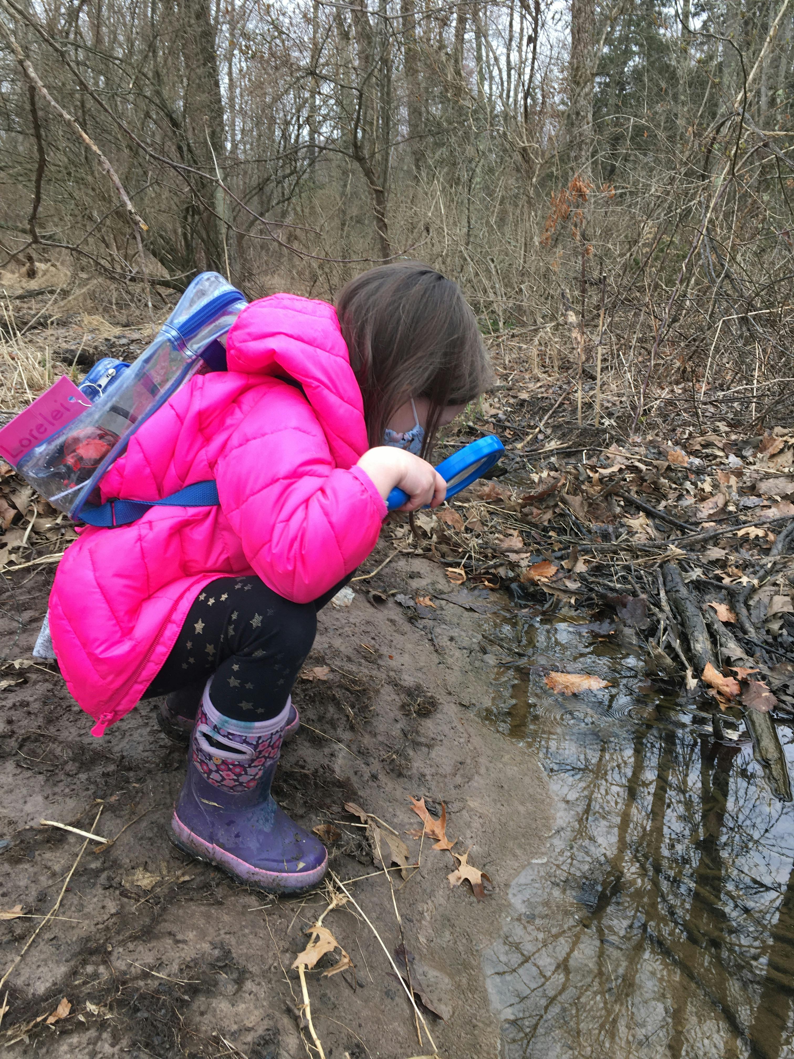 Child crouching by water with a blue object in a wooded area