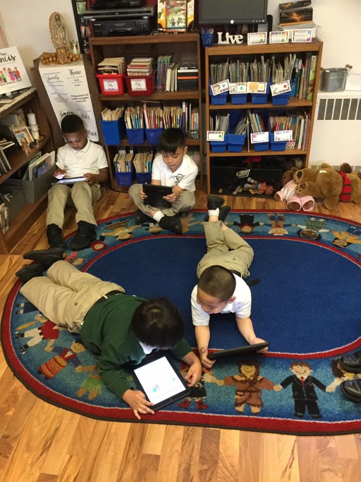 Four children using tablets on a rug in a classroom